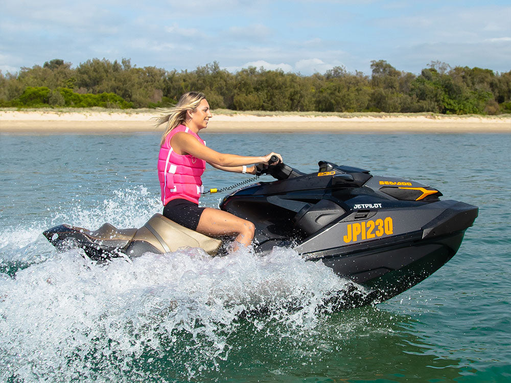Woman in pink Jetpilot Level 50S PFD riding a Sea-Doo PWC, matching Australian life jacket regulations for jet skis
