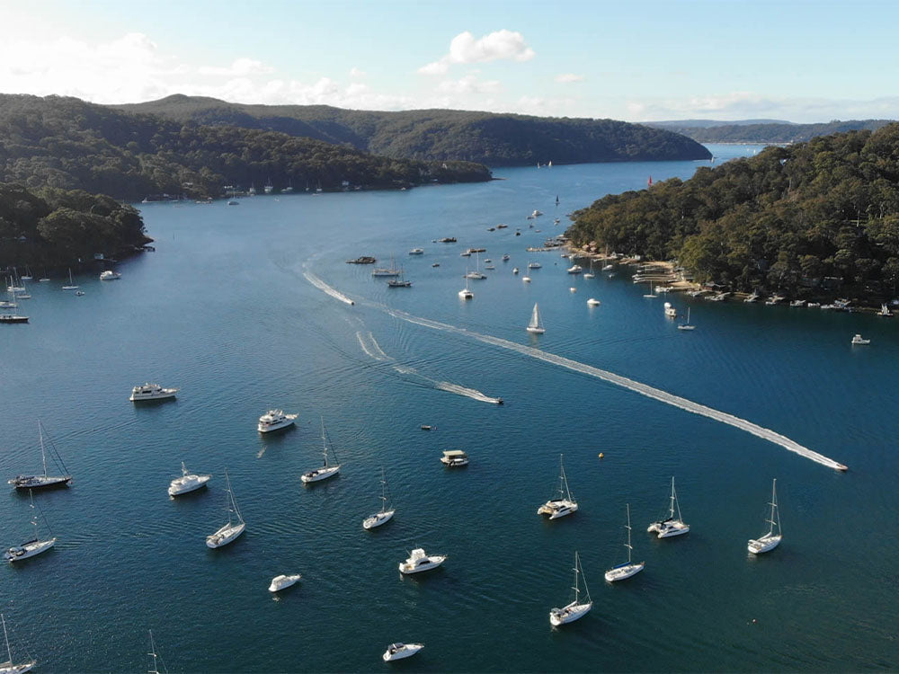 Aerial of moored boats and a PWC cutting a wake through a NSW waterway, where the PWC knowledge test rules apply