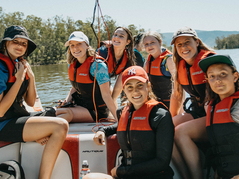 Group of teens in red Jetpilot L50S life jackets on a Nautique ski boat, showing the difference between 50 and 50S PFDs