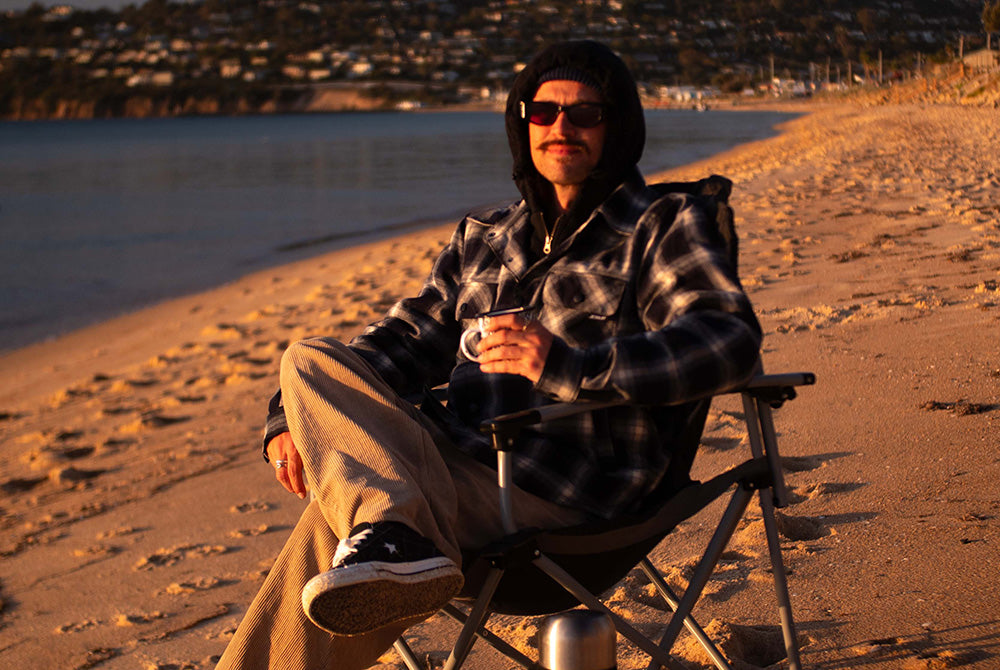 Bloke in a Jetpilot flannel jacket sipping coffee on a beach camp chair at sunset, a top flannel jacket for Aussie trips