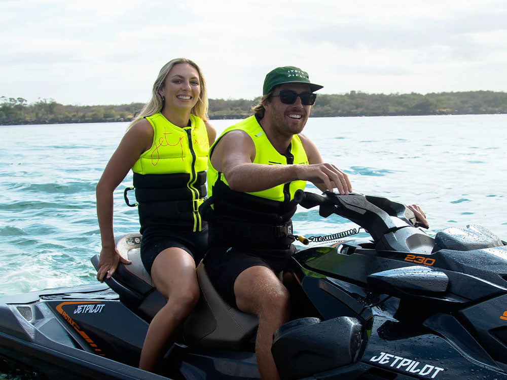 Smiling couple in hi-vis yellow Jetpilot L50S life jackets seated on a Sea-Doo Rotax 230 jet ski