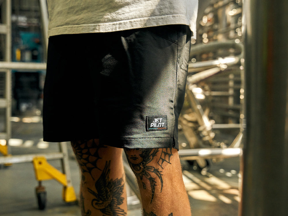 Tradie in black Jetpilot work shorts standing in an industrial workshop, showing on-knee short length