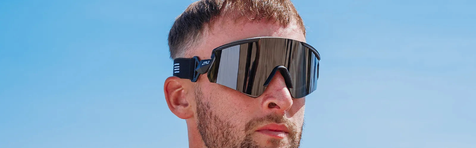 Man wearing wraparound Jetpilot floating sunglasses with mirrored lens under a clear blue sky