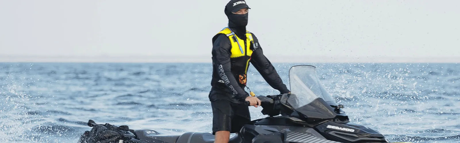 Jet ski rider in a yellow Jetpilot jet ski life jacket and balaclava launching off a Sea-Doo