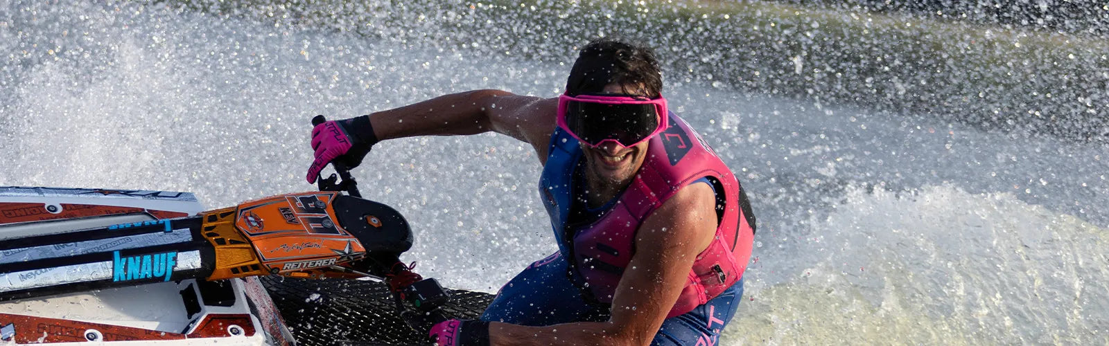 Pro jet ski racer in pink Jetpilot goggles and PFD throwing spray on a stand-up ski