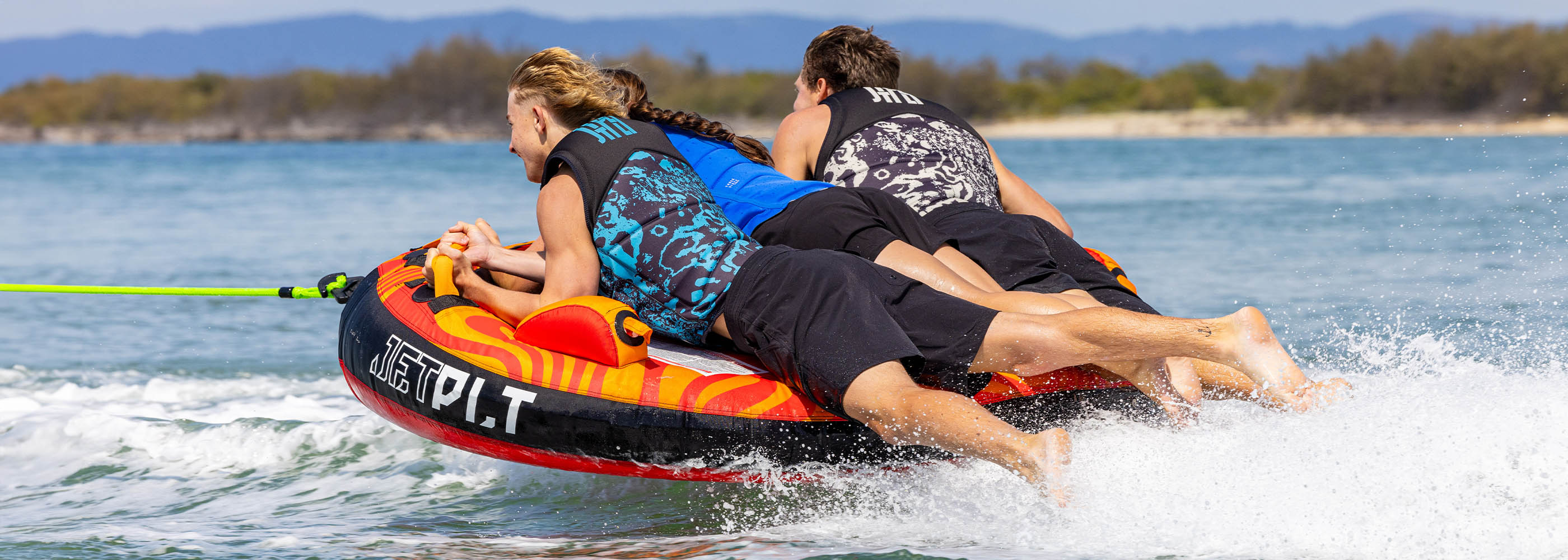 Two riders being towed across the water on a Jetpilot inflatable towable tube behind a boat