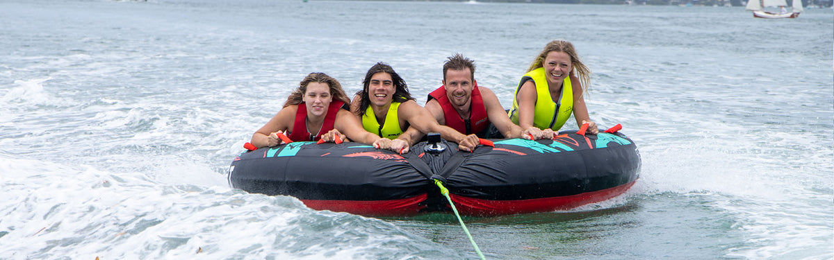 Four people in yellow life jackets riding a Jetpilot 4 person ski tube behind a boat