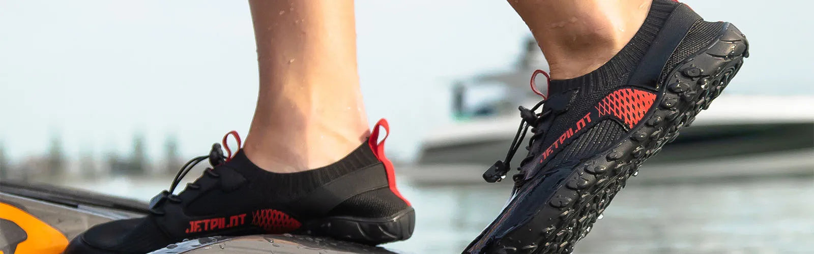 Close-up of feet wearing black and red Jetpilot water shoes on a jet ski deck above the water