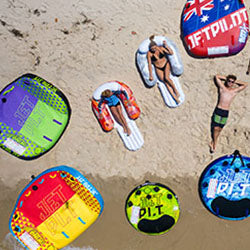 Aerial view of colourful Jetpilot ski tubes and people relaxing on inflatable loungers on a sandy beach