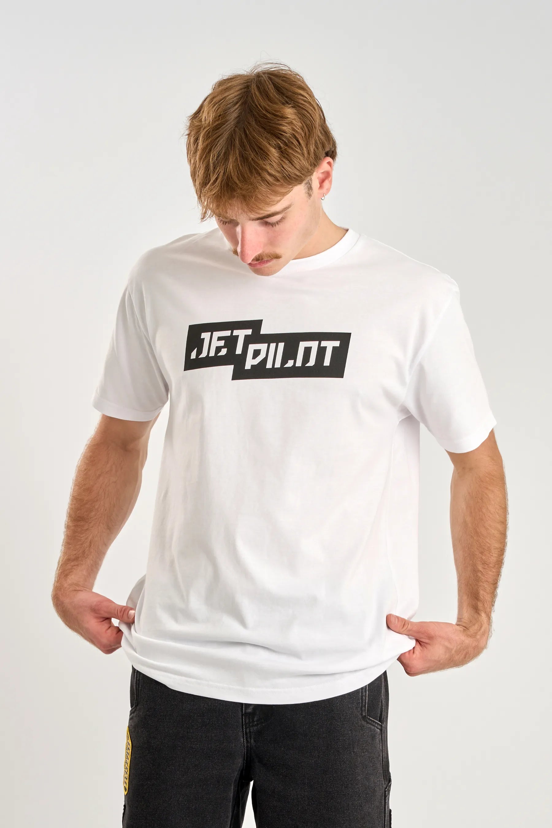 Person wearing a white t-shirt with 'Jetpilot' logo on a plain background