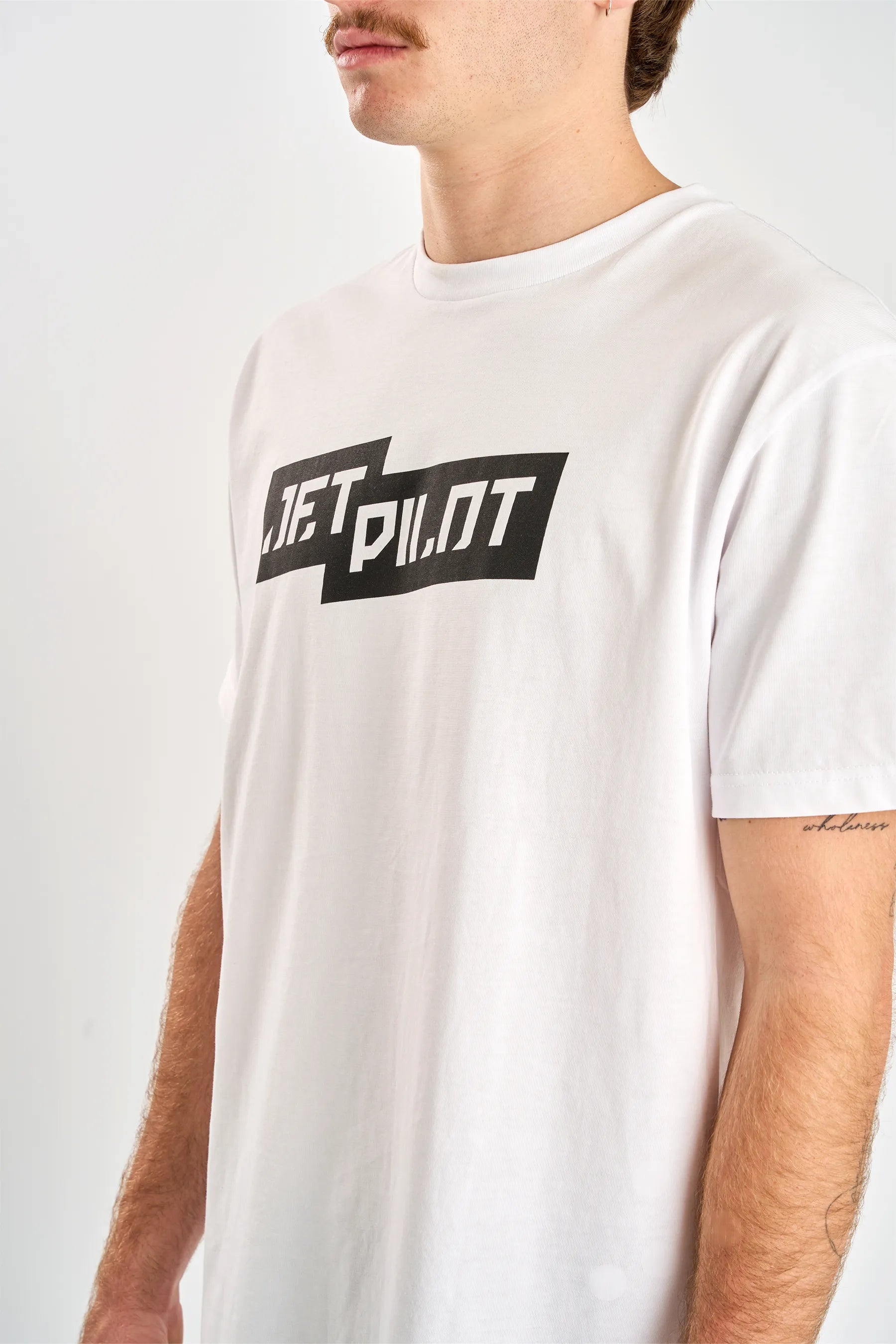 Person wearing a white t-shirt with 'Jetpilot' logo on a plain background