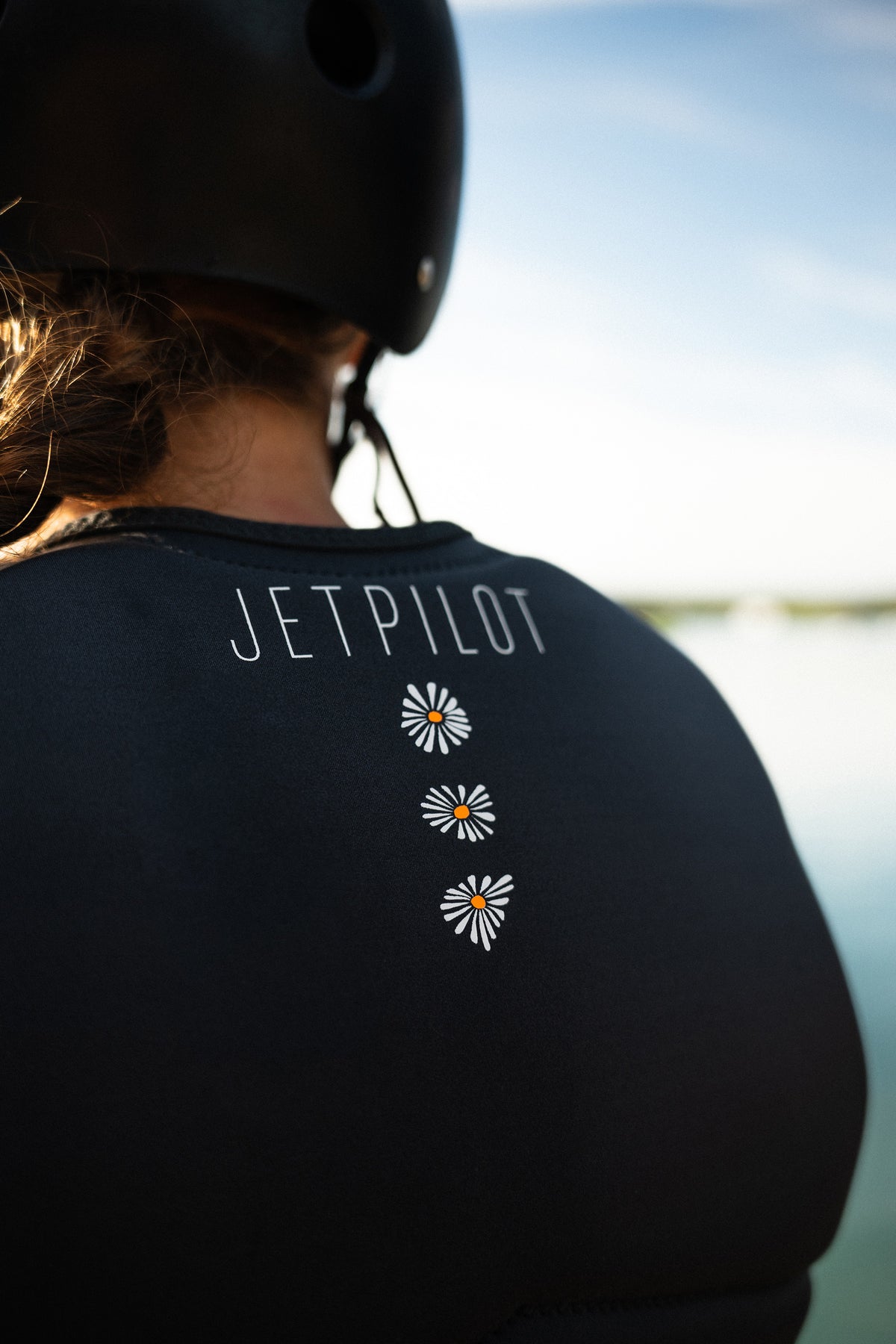 Back of a rider in a helmet wearing the Charcoal Isla, showing the Jetpilot name and three daisies