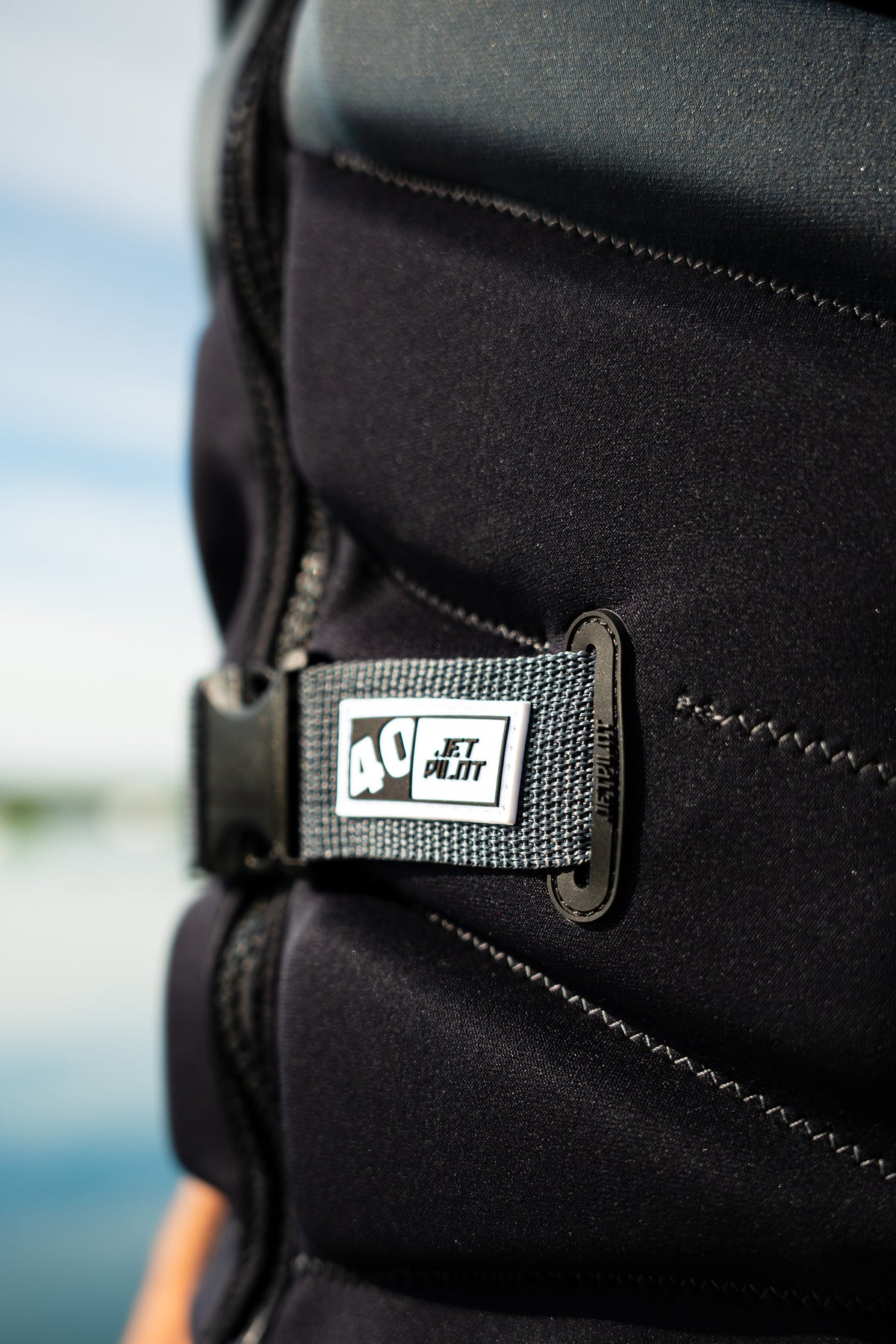 Close-up of the 40 tab on the waist buckle of the Charcoal Isla, worn by a rider by the water