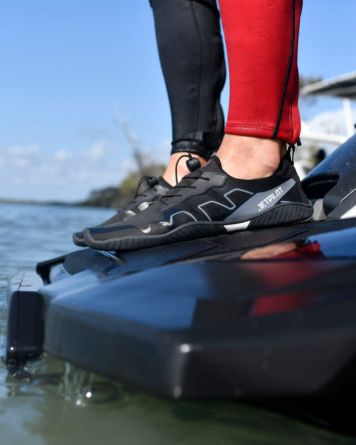 Person wearing black shoes with white accents standing on a black platform over water.