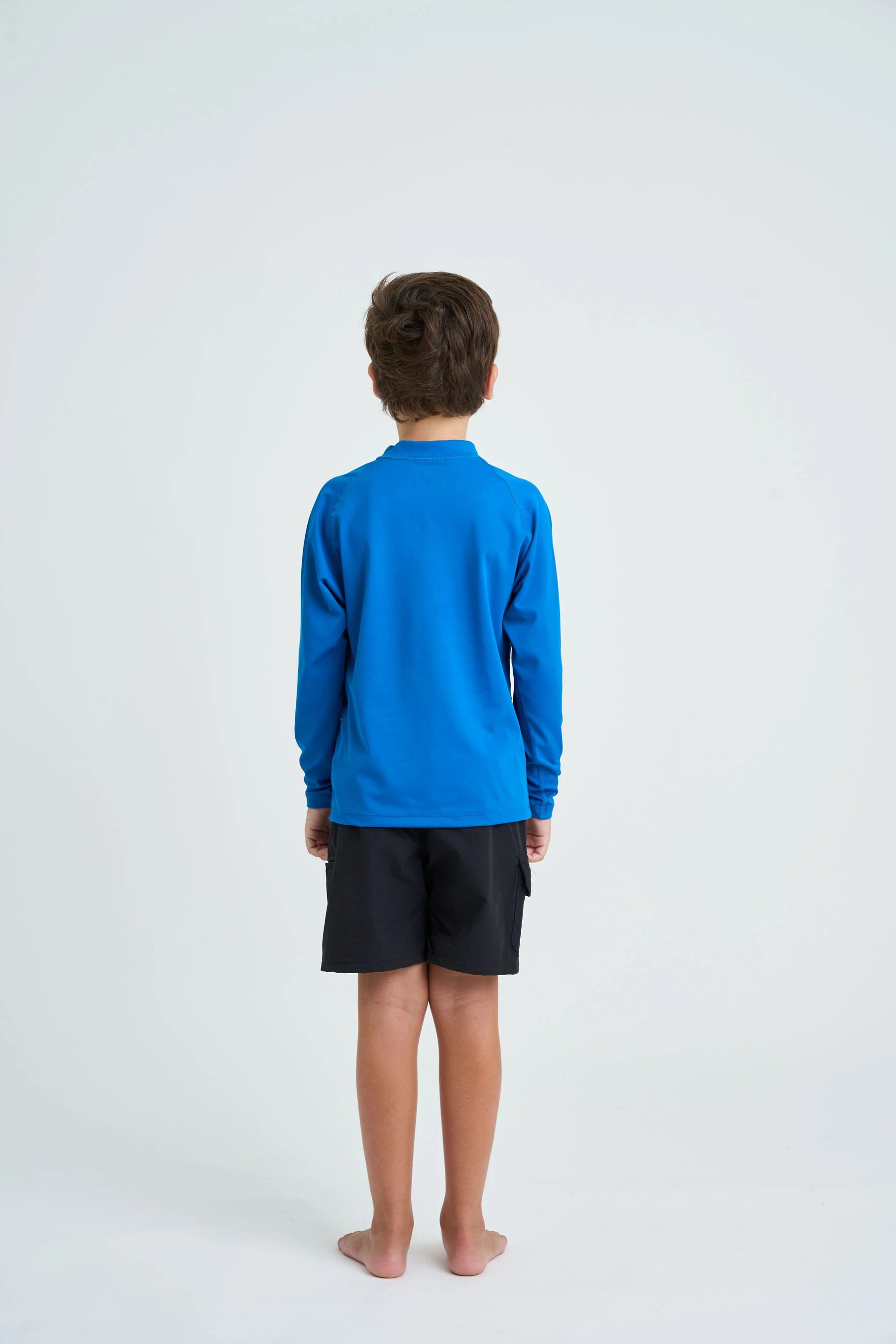 Child wearing a blue long-sleeve shirt and black shorts on a white background
