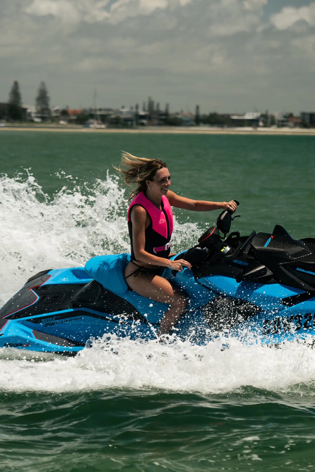 Rider riding a jet ski through spray on the water in the Pink Cause Ladies life jacket