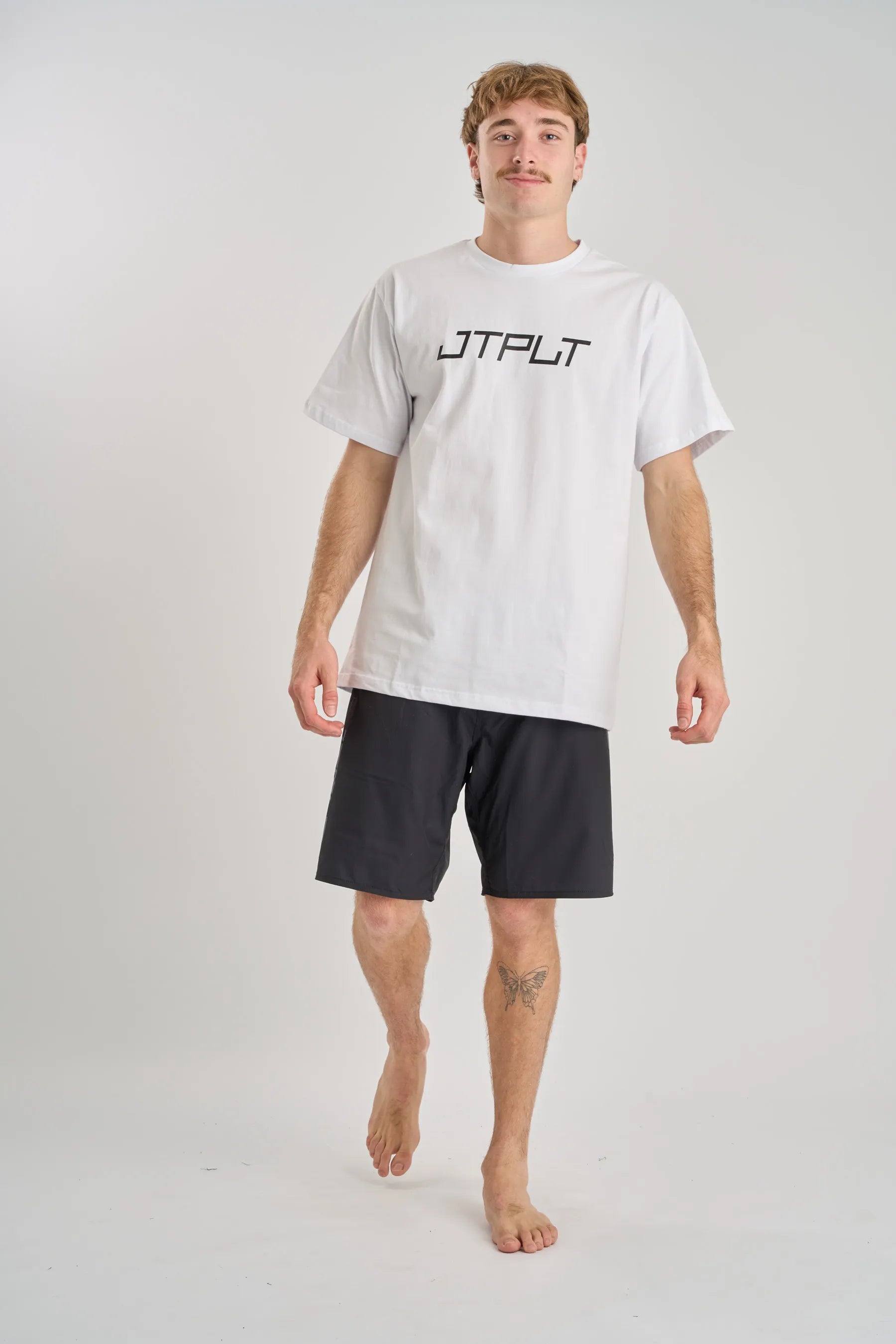Person wearing a white t-shirt with 'JTPLT' logo and black shorts on a light gray background