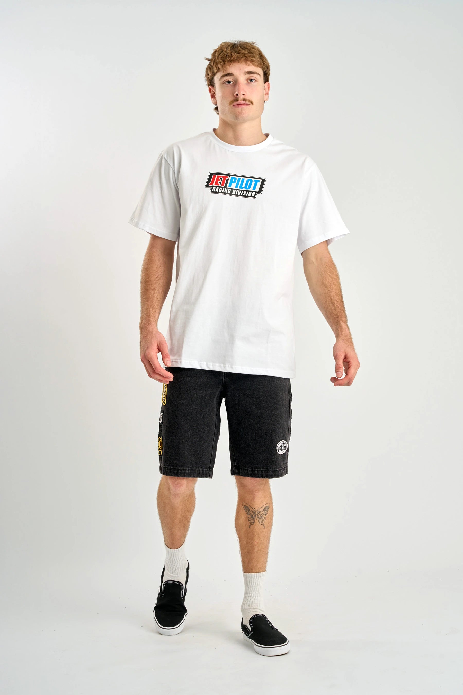 Person wearing a white t-shirt with a logo and black shorts on a white background — image 2
