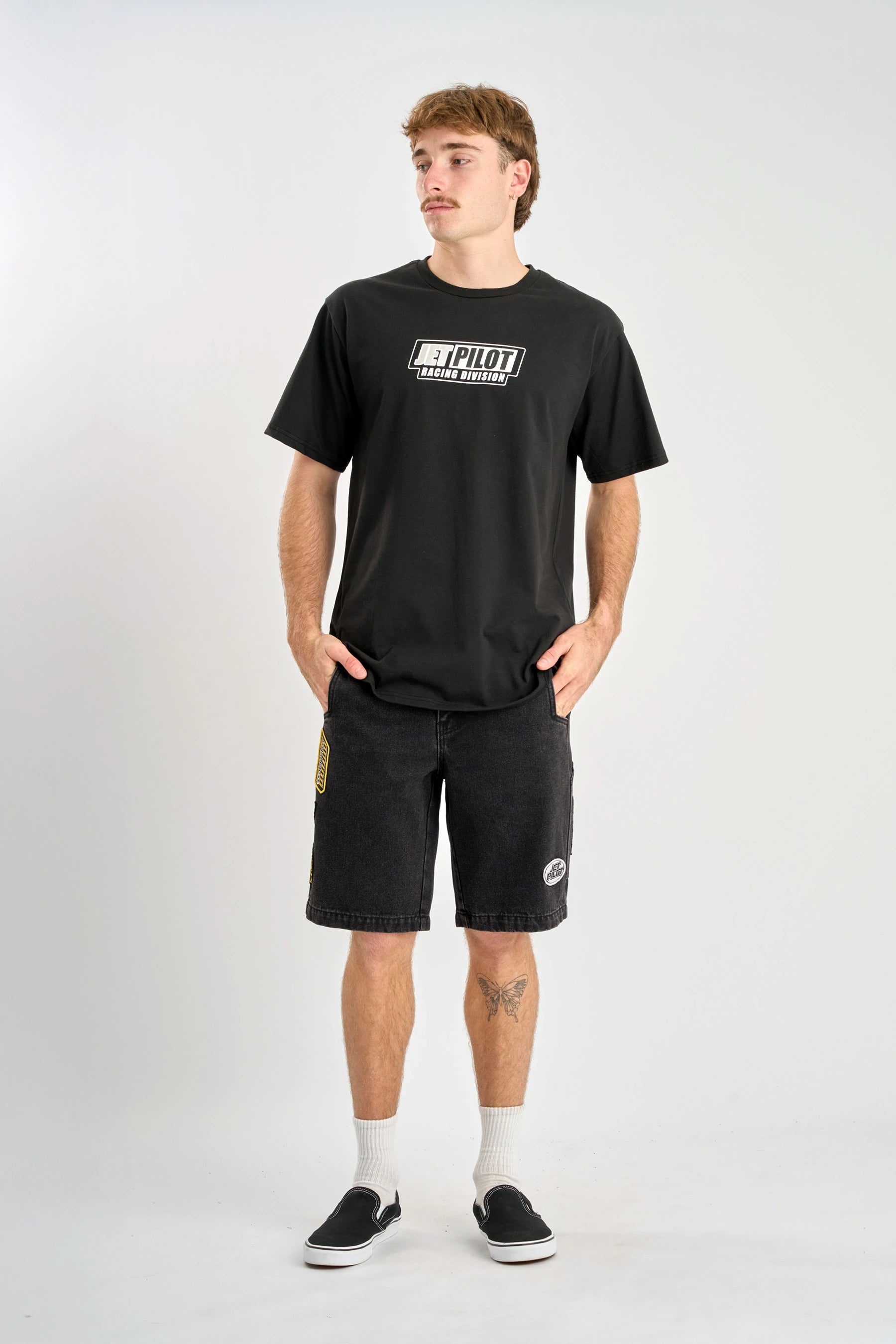 Person wearing a black t-shirt with a logo and black shorts on a white background — image 3
