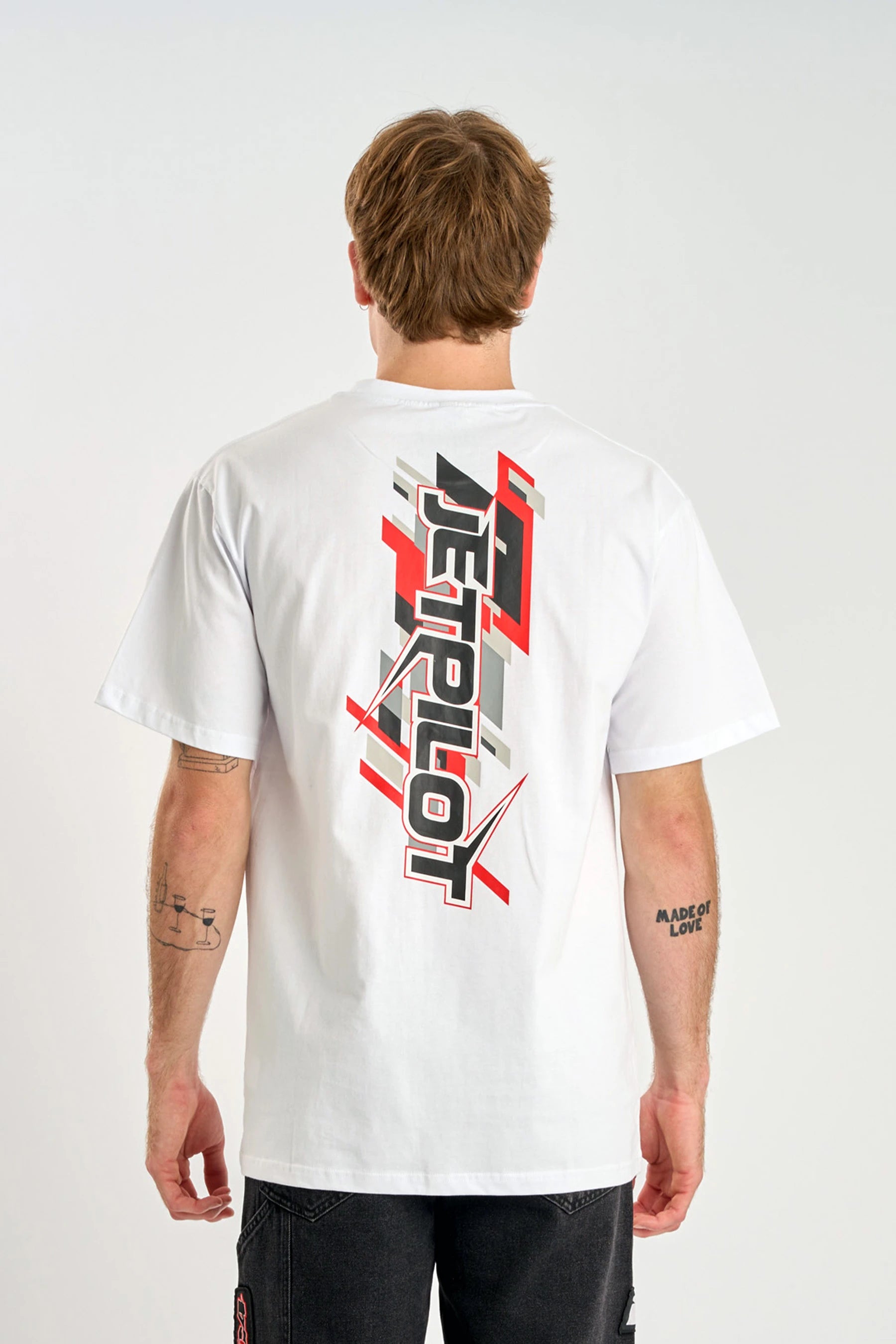 Person wearing a Jetpilot Raptor Tee - White t-shirt with a red and black logo on the back, standing against a plain backgrou