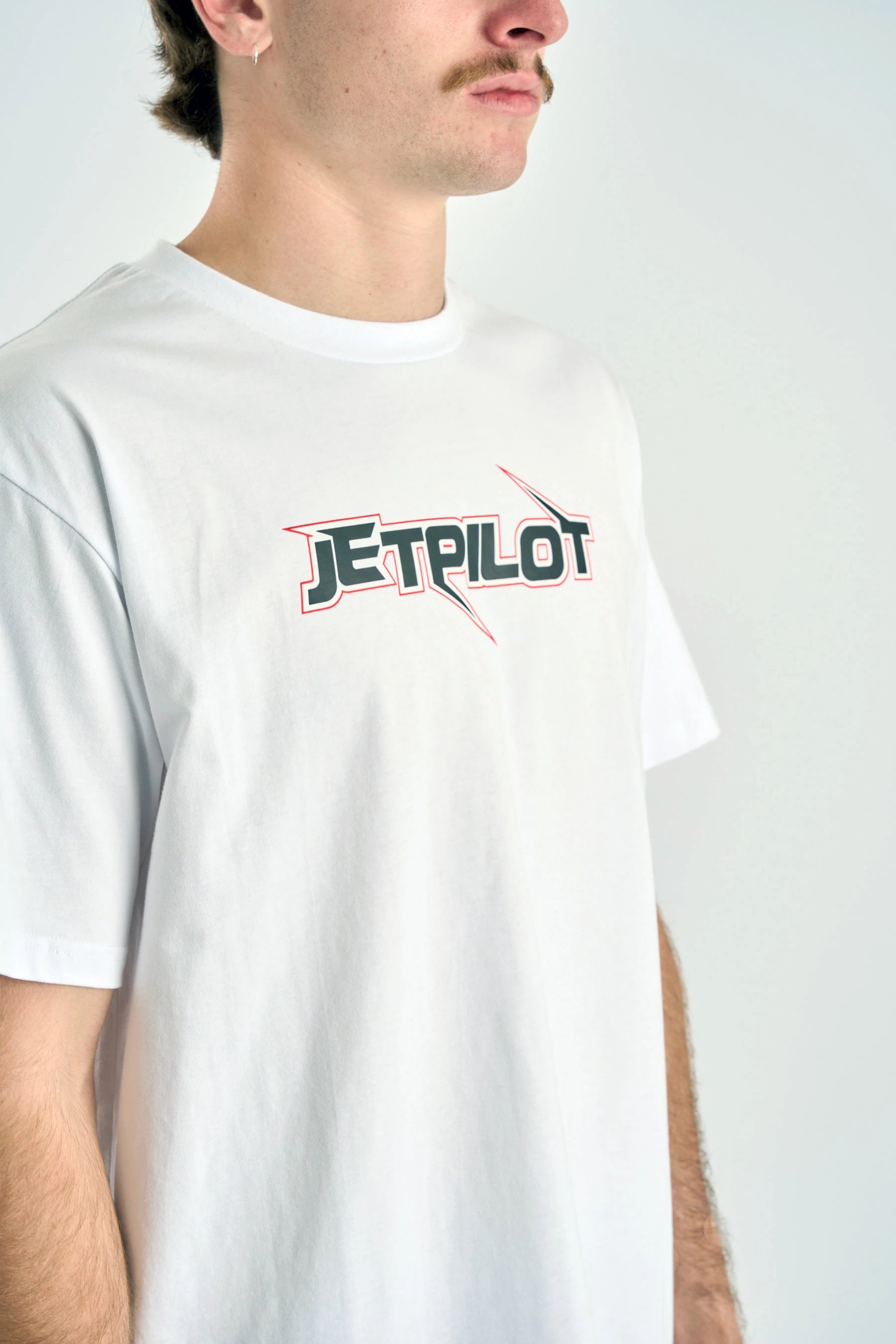 Person wearing a white t-shirt with 'Jetpilot' logo on a plain background — image 6