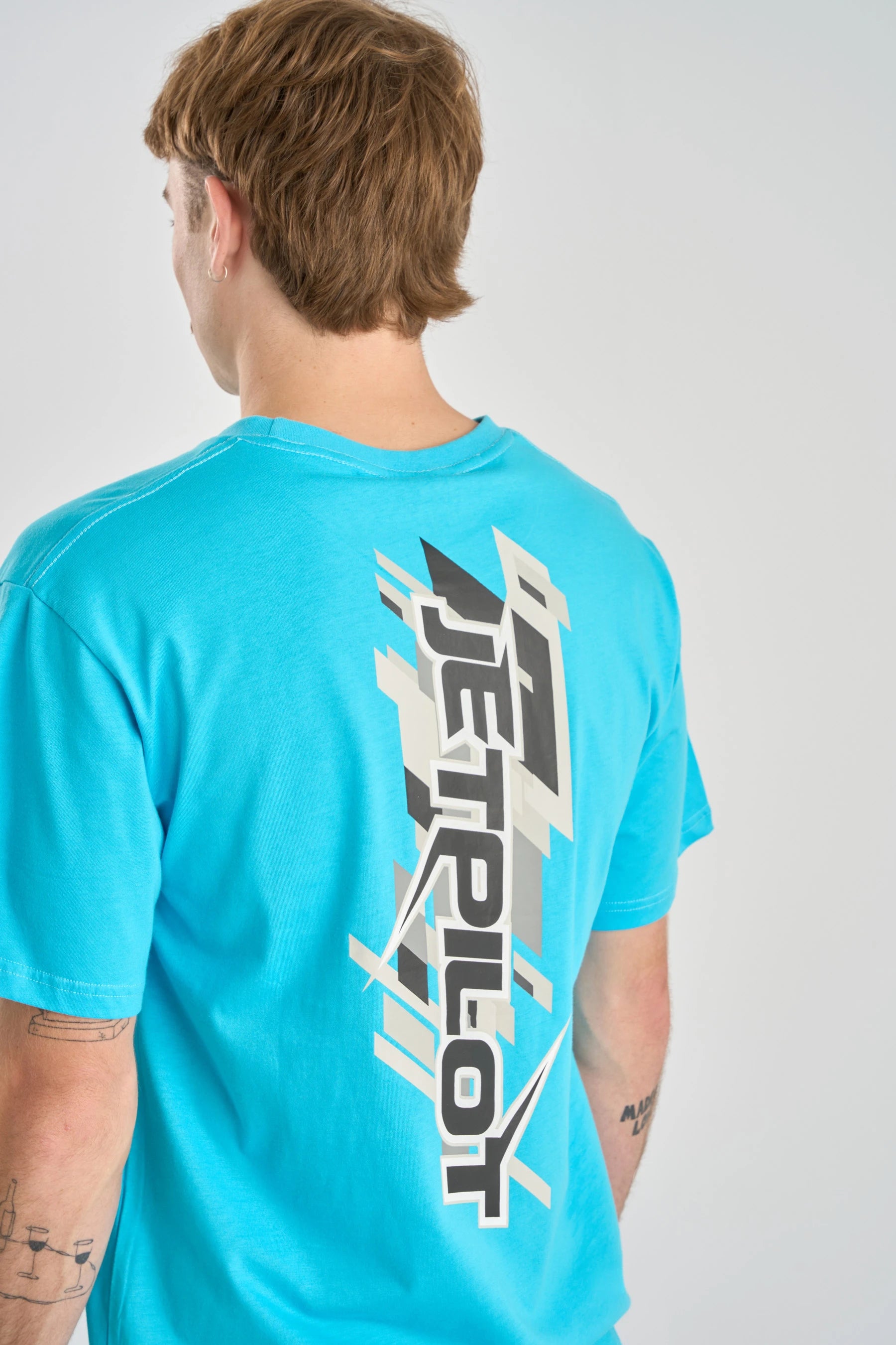 Person wearing a turquoise t-shirt with a logo on the back against a white background — image 2