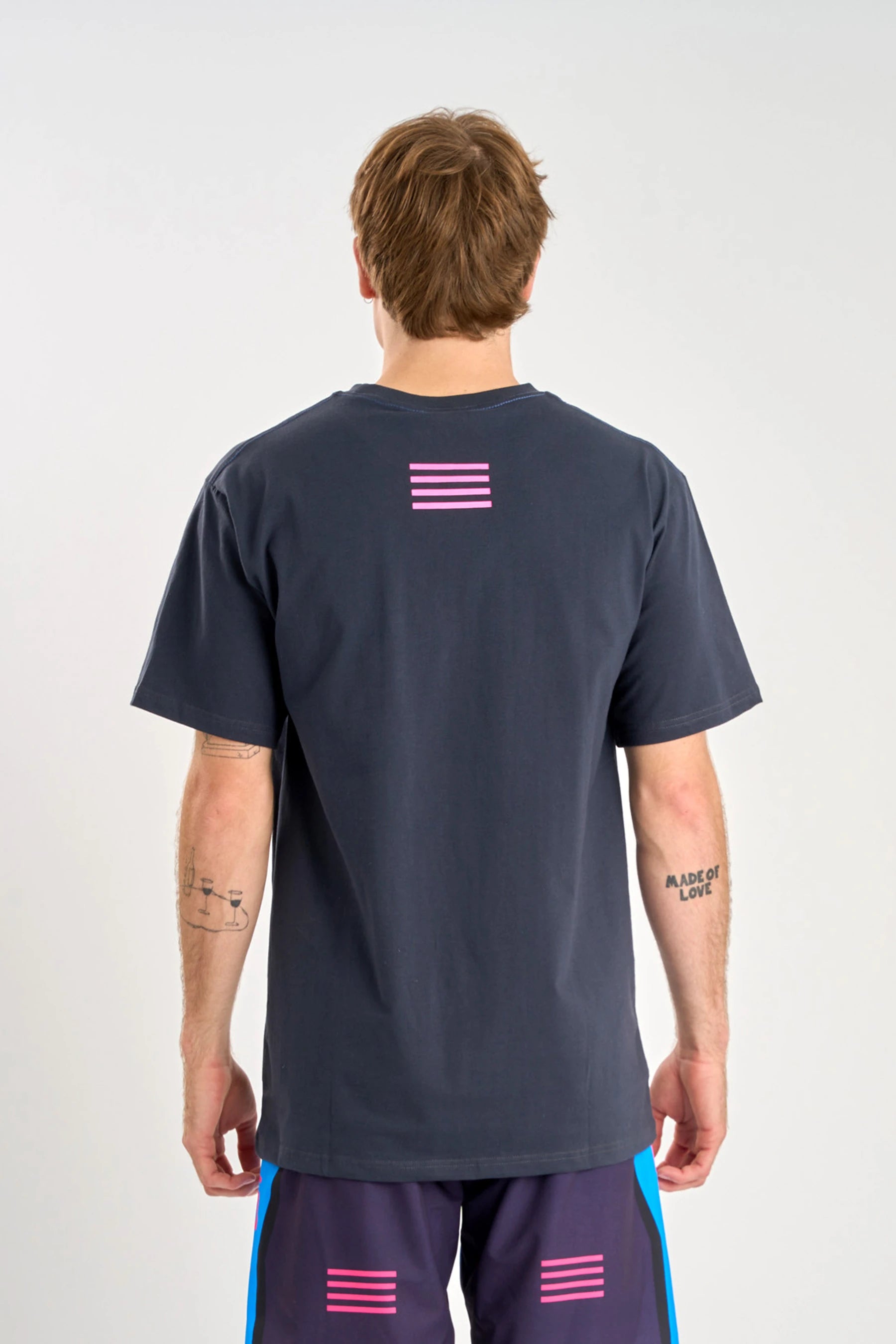 Person wearing a Jetpilot Vault SS Tee - Navy t-shirt with a pink flag design on the back, standing against a white backgroun