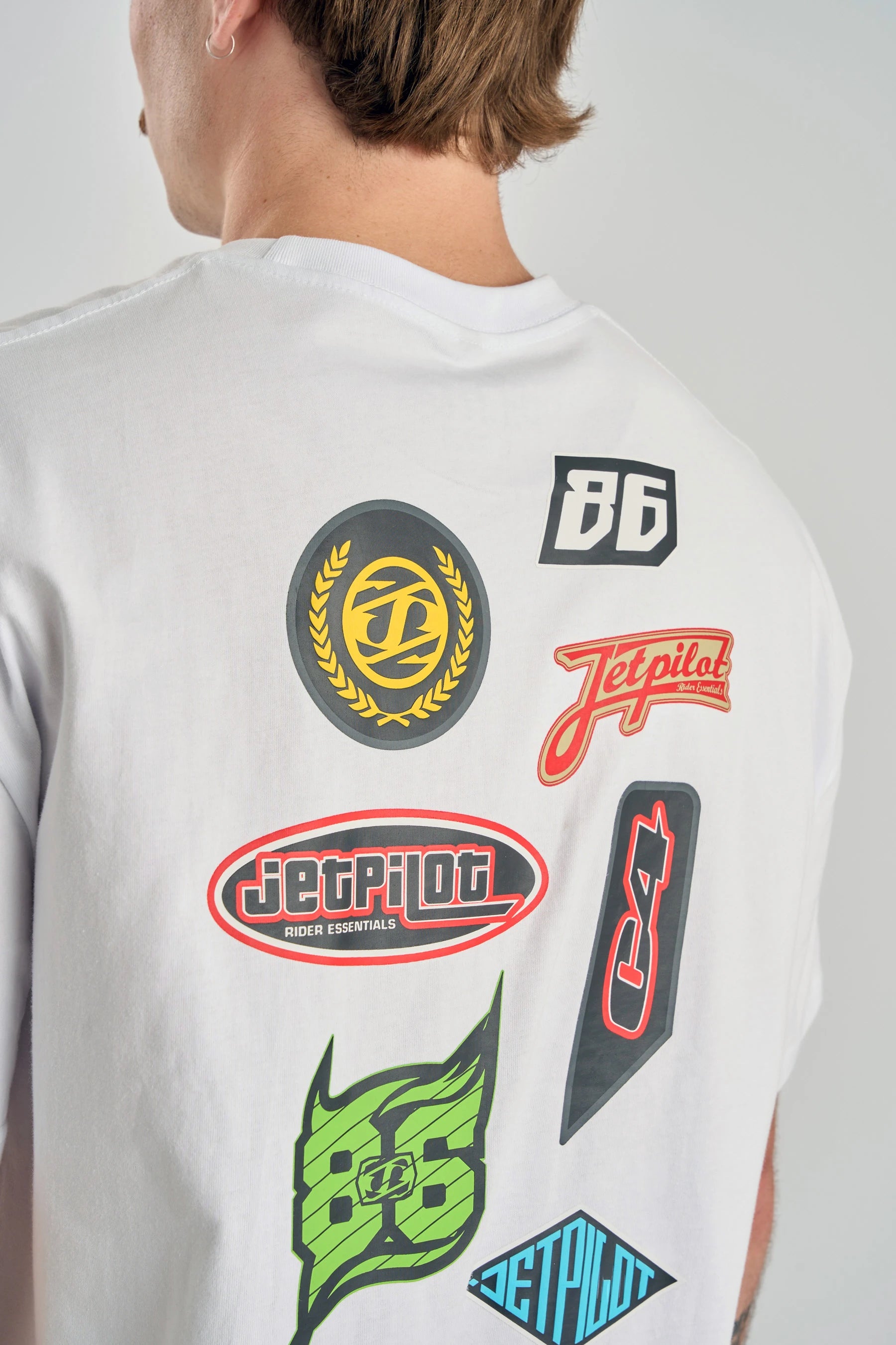 Person wearing a Jetpilot Factory Heavy Tee - White with various colourful logos on the back. — image 2