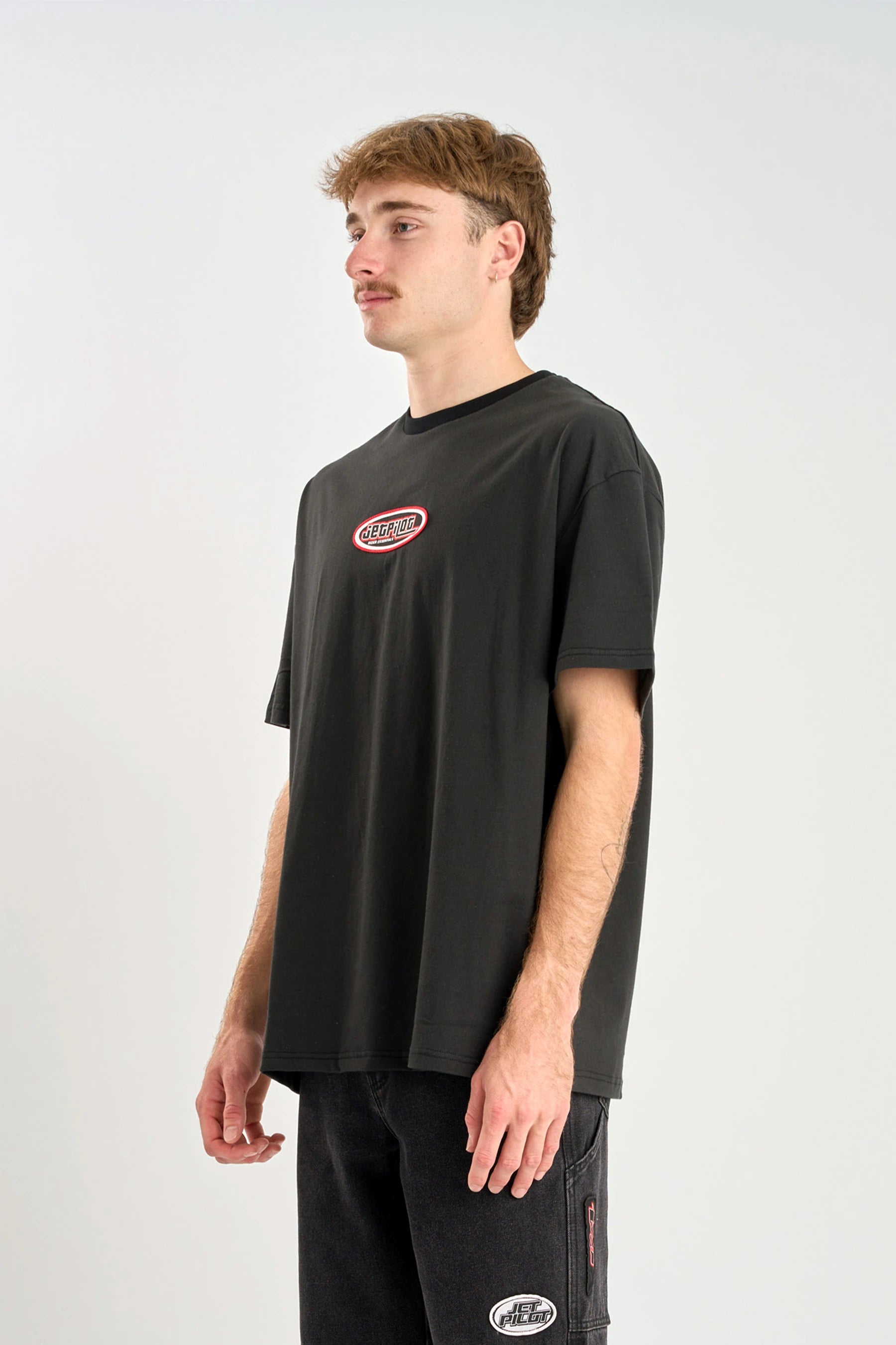 Person wearing a Jetpilot Factory Heavy Tee - Black t-shirt with a logo on a white background — image 2