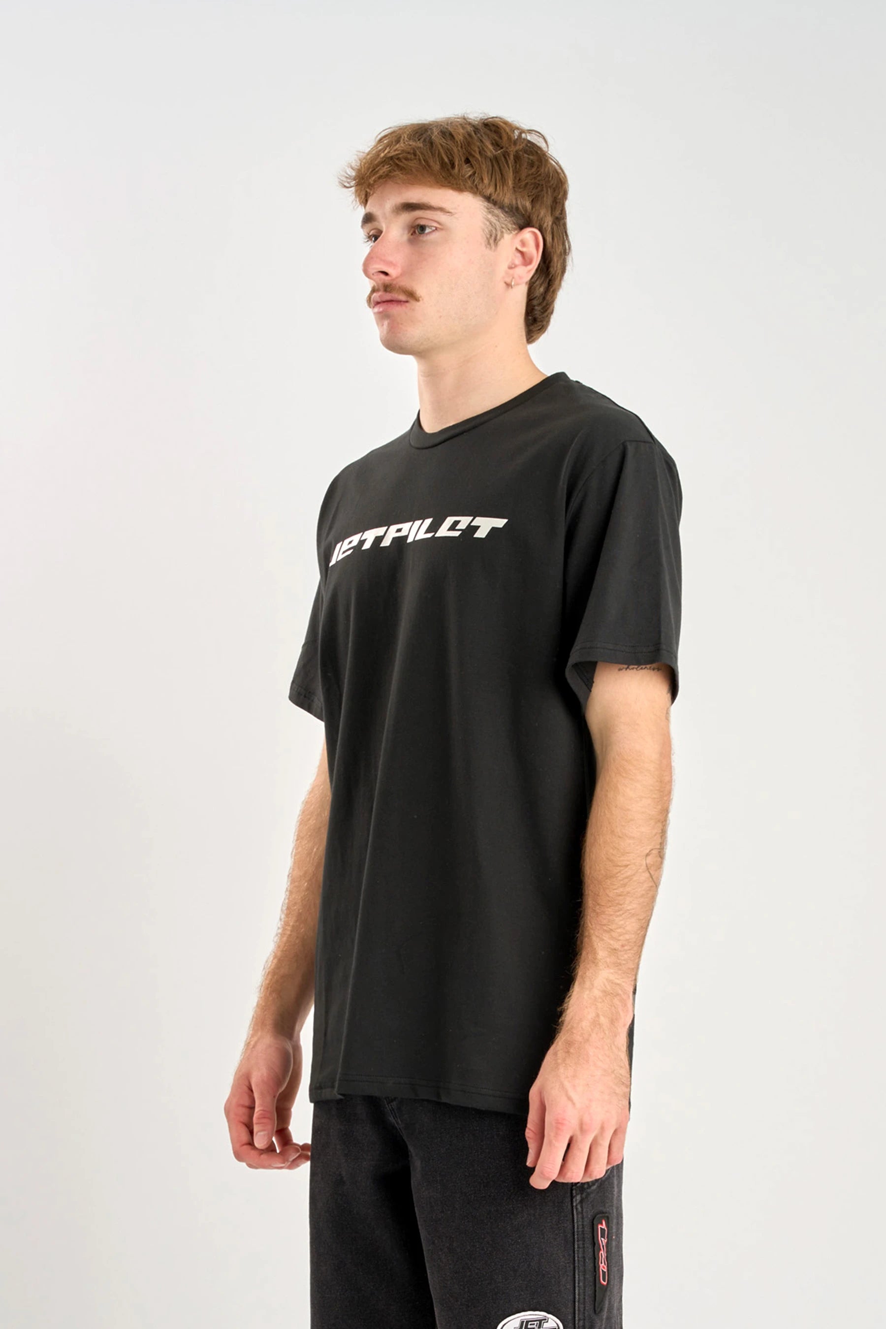 Person wearing a black t-shirt with 'Jetpilot' branding on a white background — image 2
