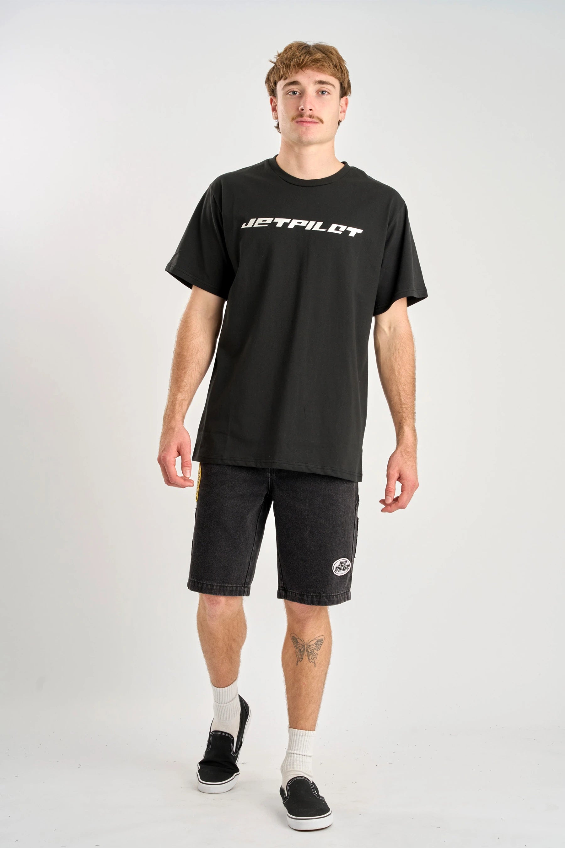 Full body image of man wearing a black t-shirt with 'Jetpilot' logo and black shorts on a white background — image 2