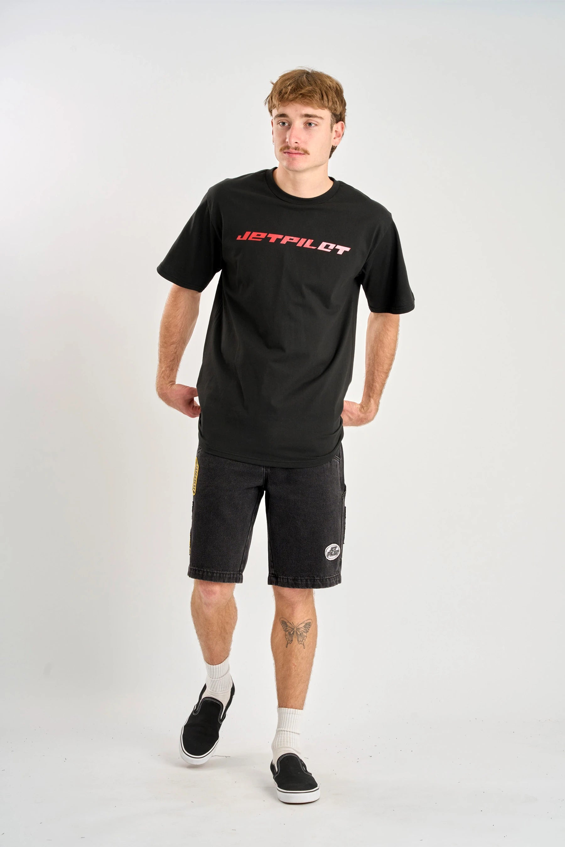 Person wearing a black and red 'Jetpilot' logo t-shirt and shorts on a white background — image 2