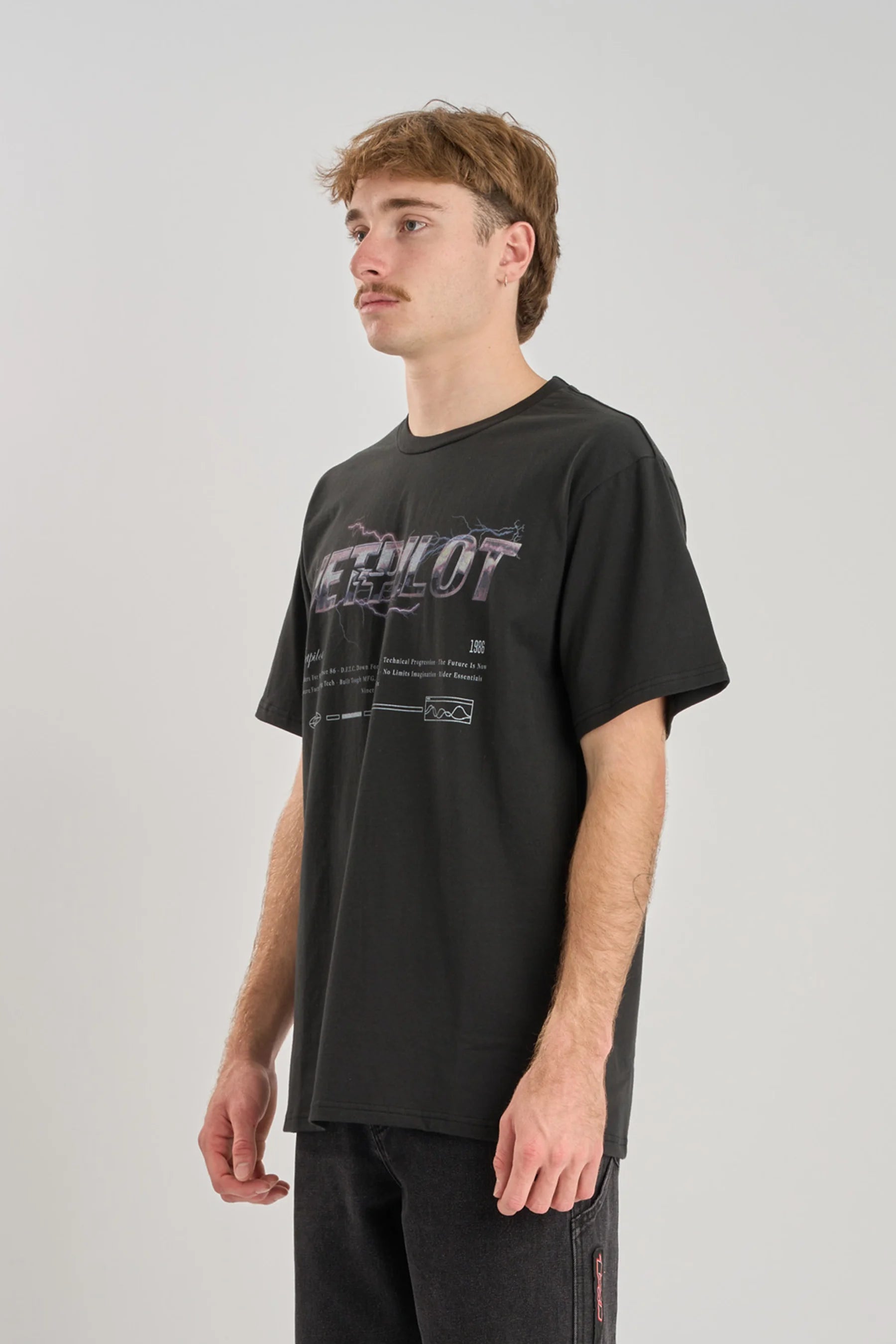 Person wearing a black Jetpilot t-shirt with lightning graphic on a plain background