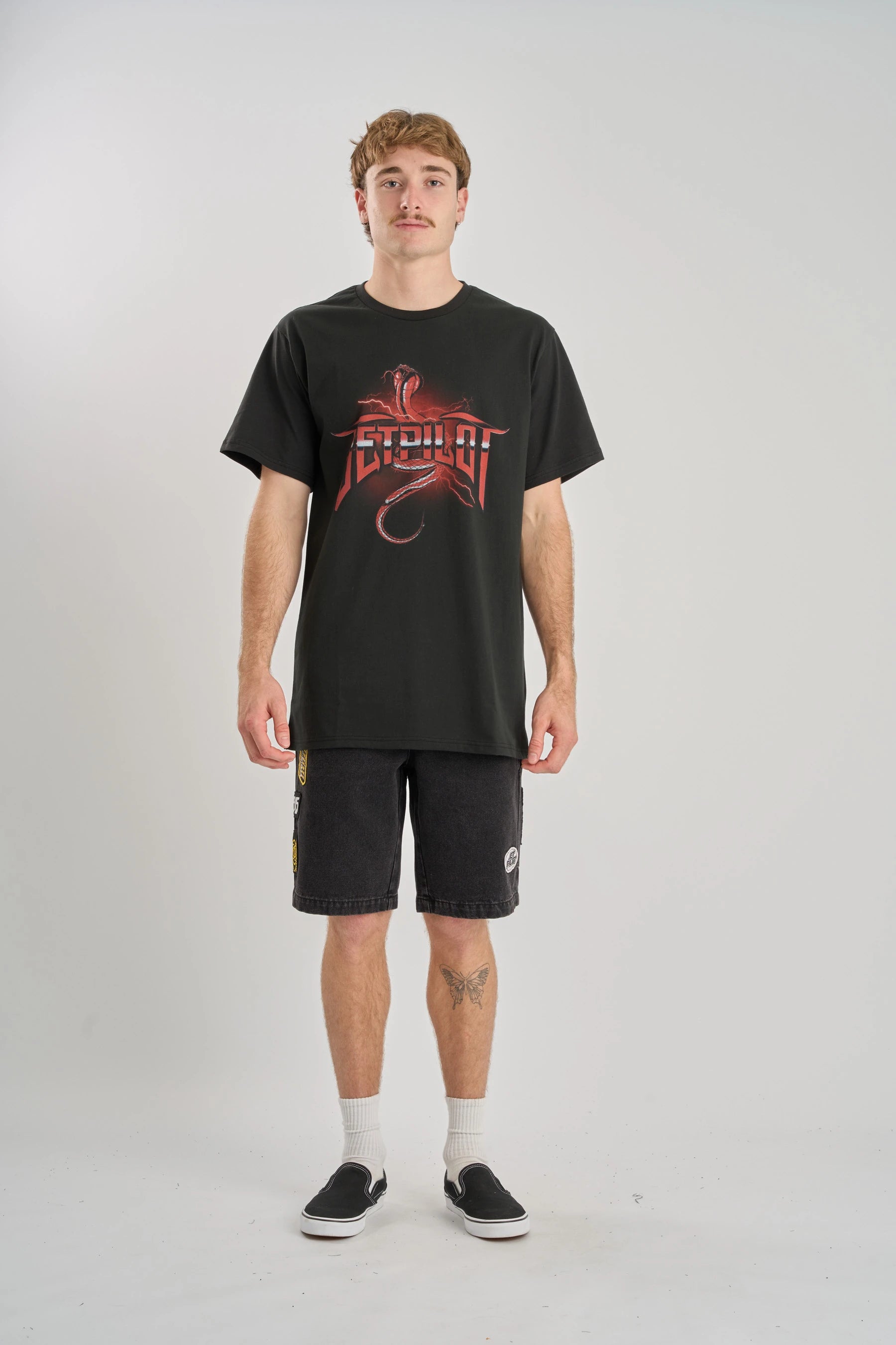 Person wearing a black t-shirt with a red logo and black shorts on a white background — image 2
