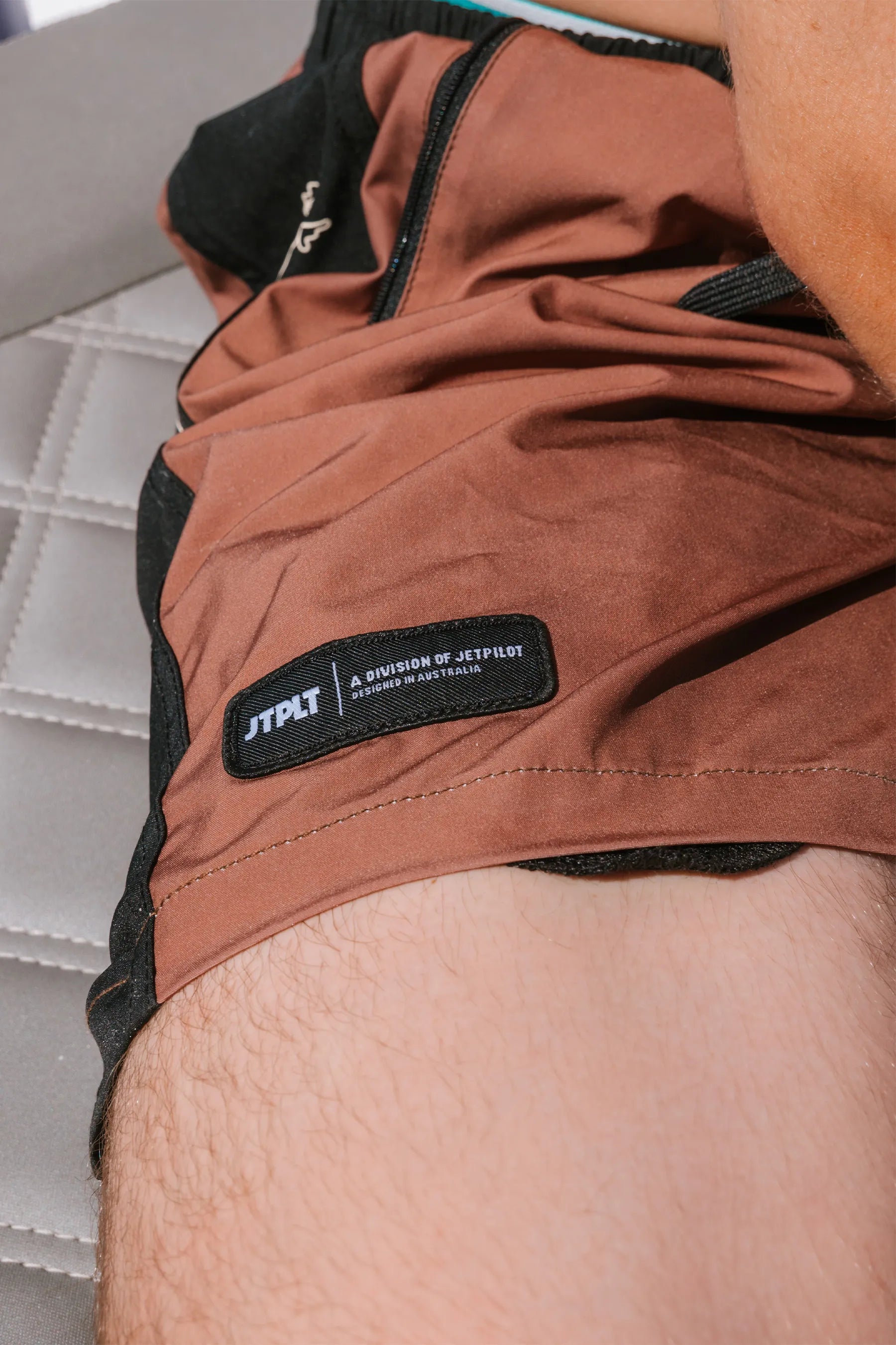 Jetpilot Chicken Boardshorts - Brown up close image of black embroidered label on front corner of boardshorts - neutral background