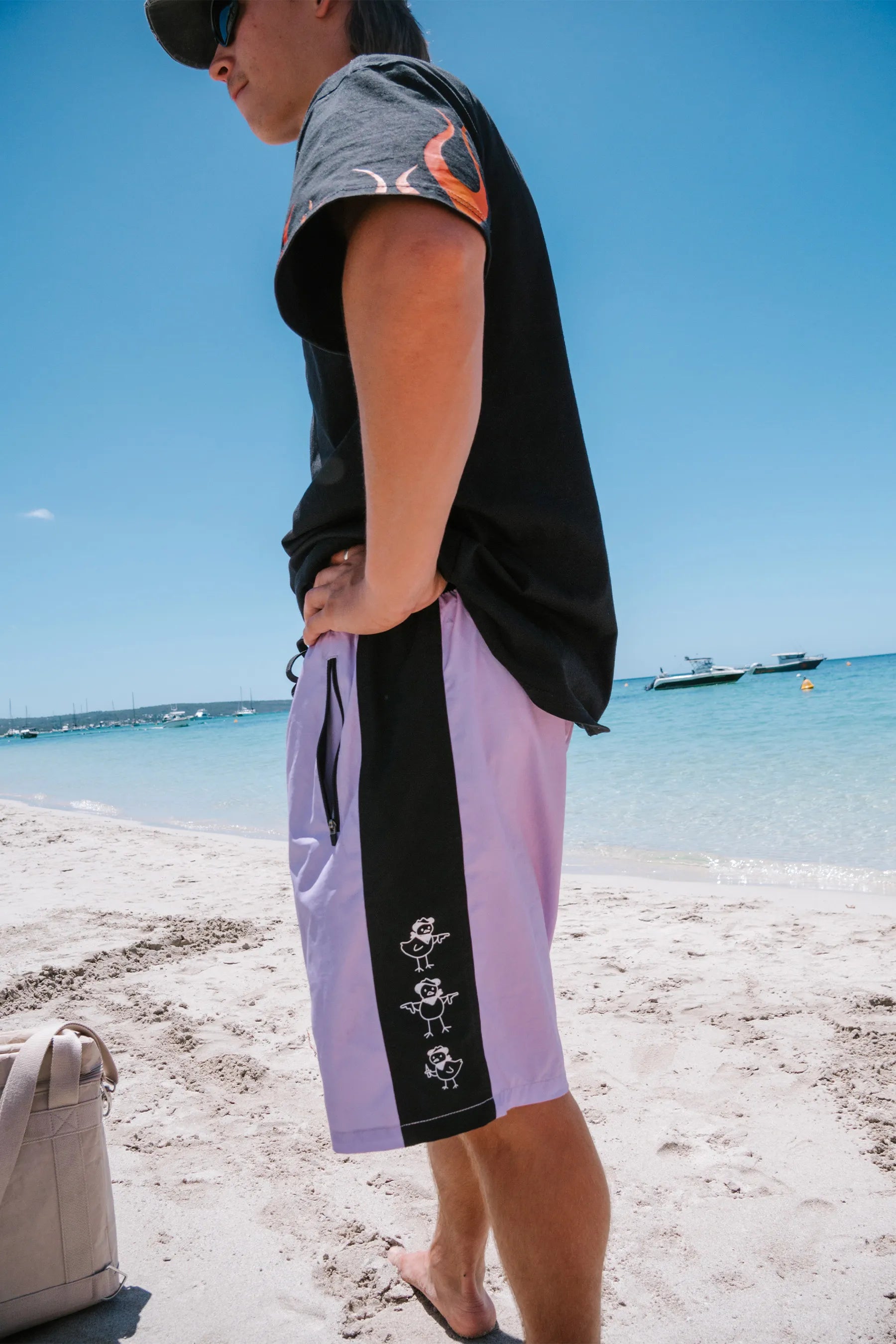 Person wearing a black and gray sleeveless shirt and light purple shorts with black trim on a beach.