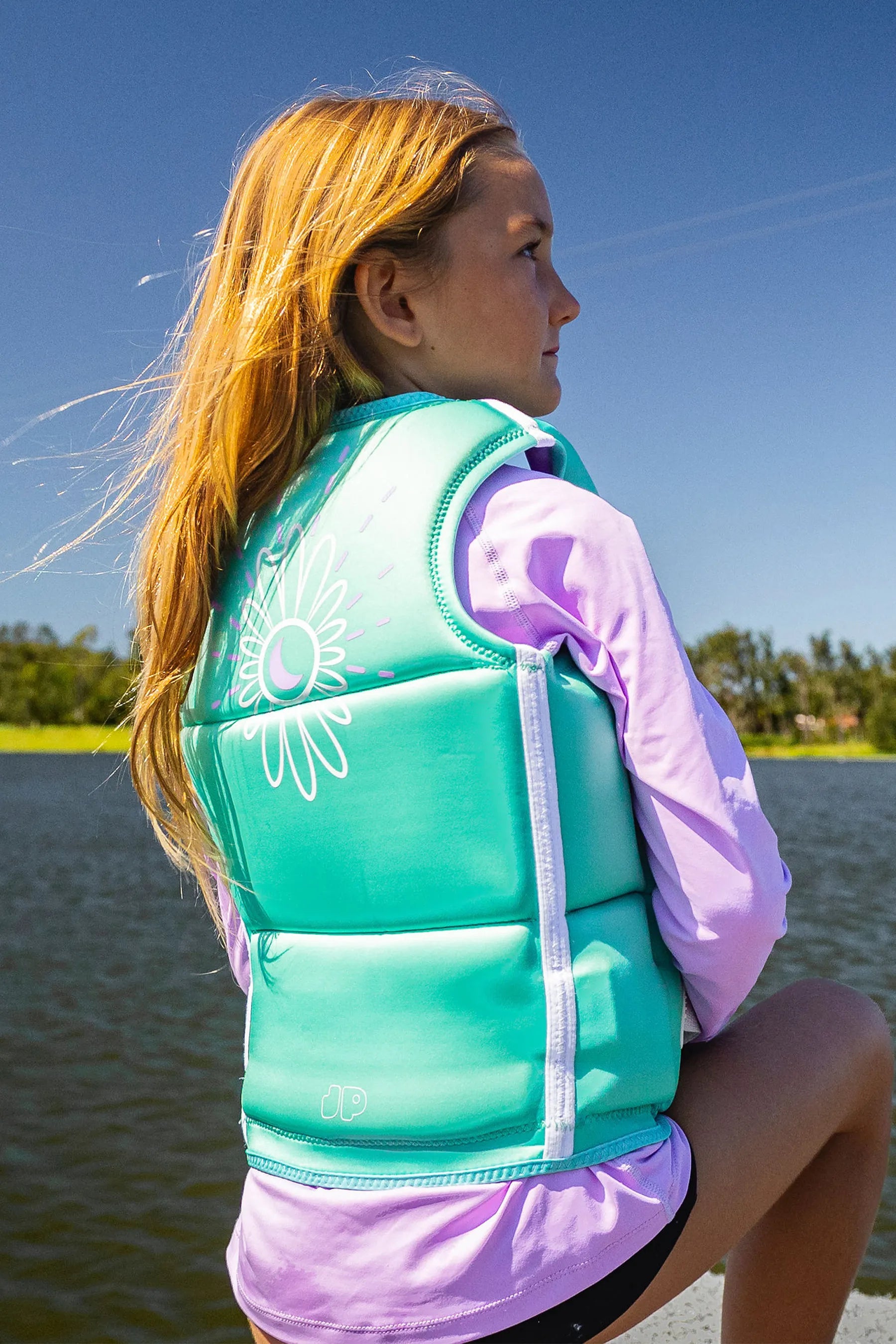Person wearing Jetpilot Freeride Girls Life Jacket - Teal and pink shirt by a body of water.