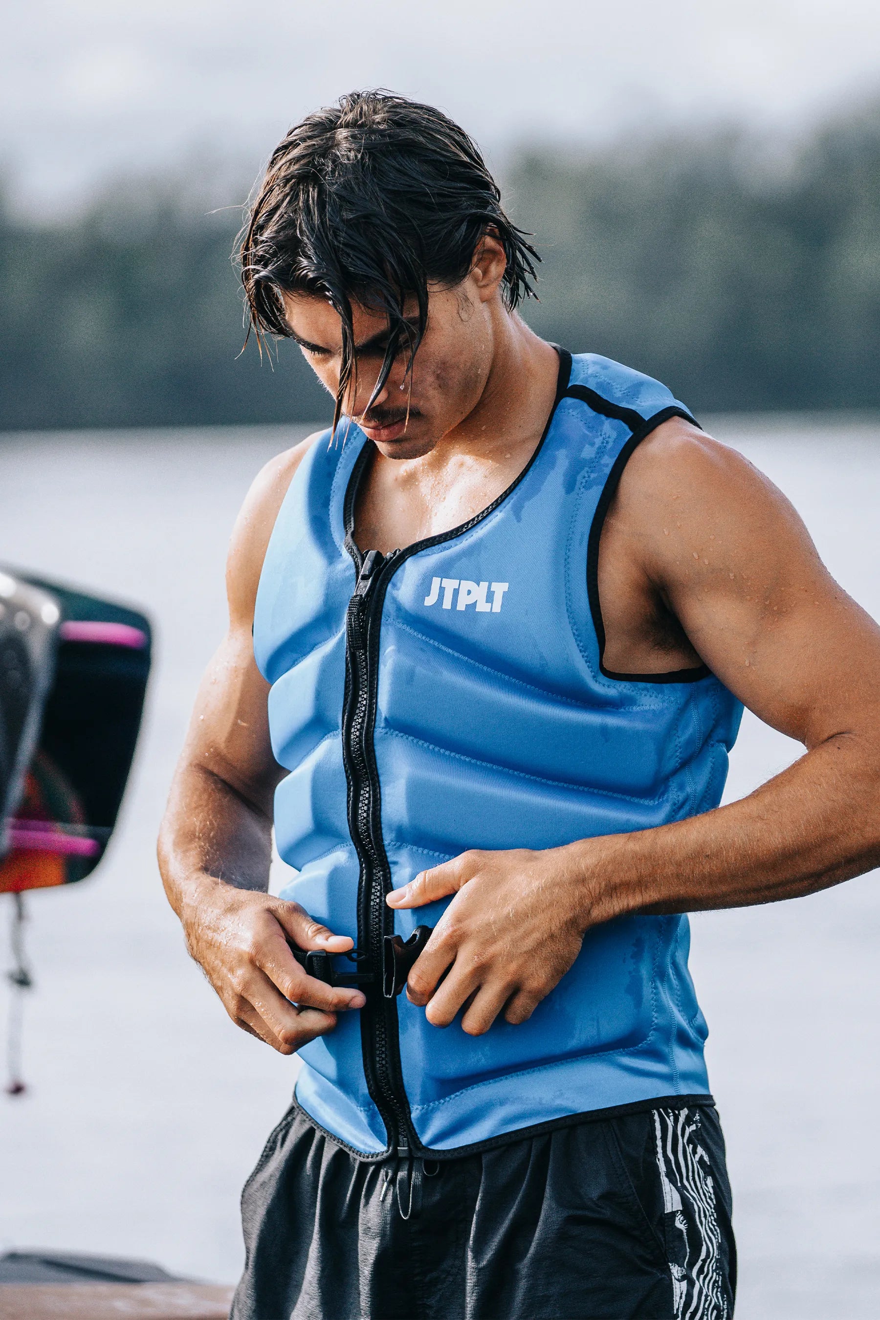 Person wearing a Jetpilot Freeride Life Jacket - Blue with 'JTPLT' branding by a body of water.