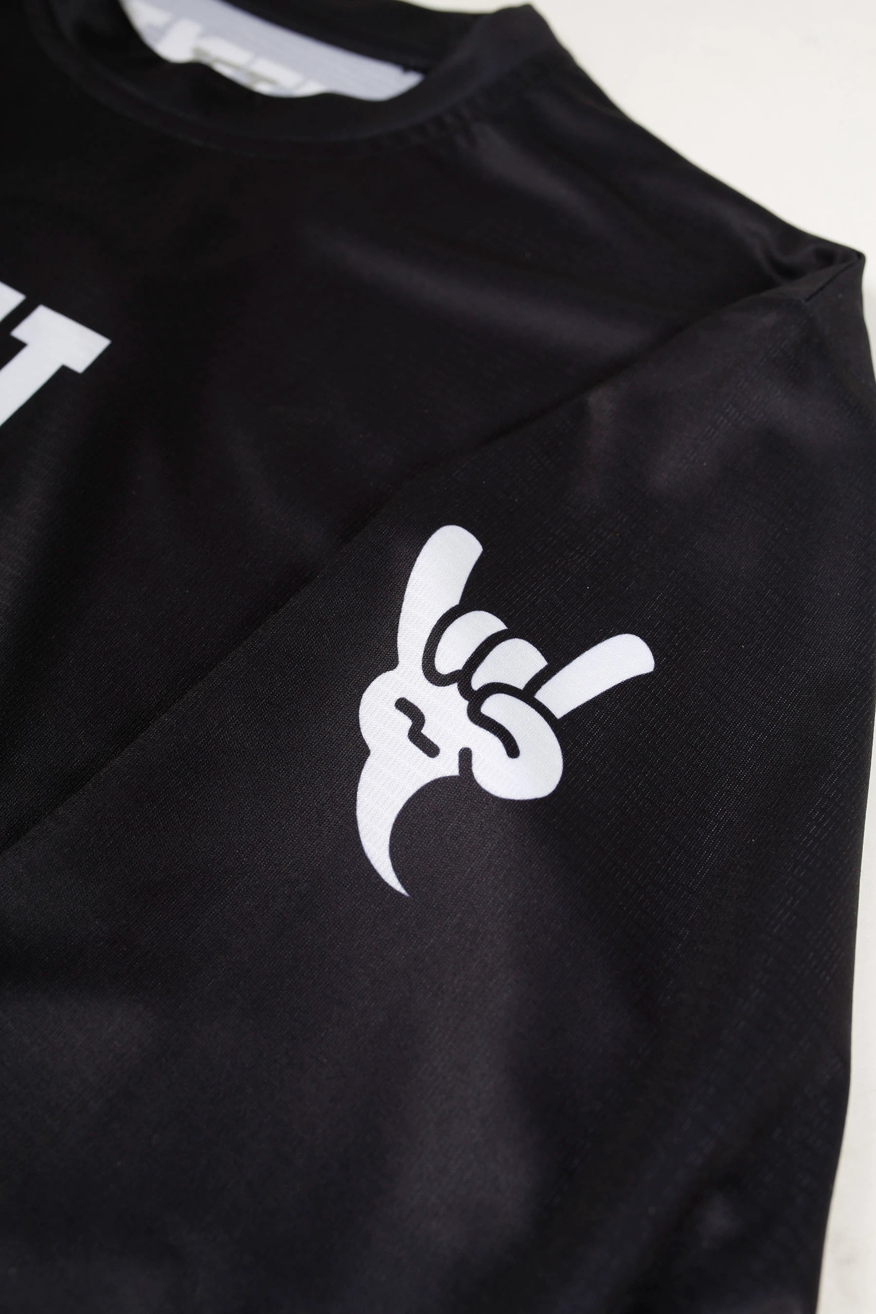 Black rash shirt with white "shaka" logo on a light gray background