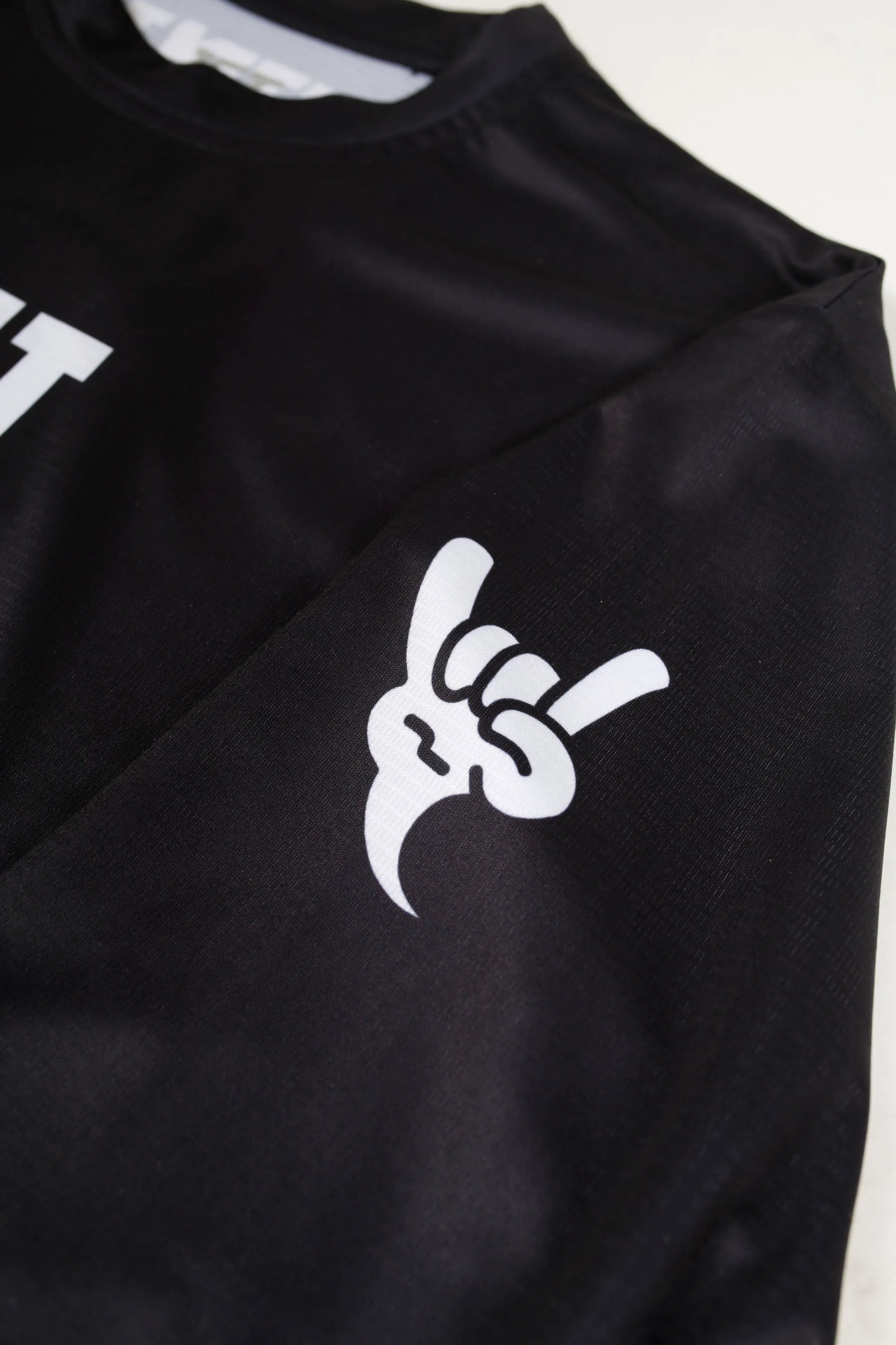 Black sun protection rash shirt with a white "Shaka" graphic design on a light gray background