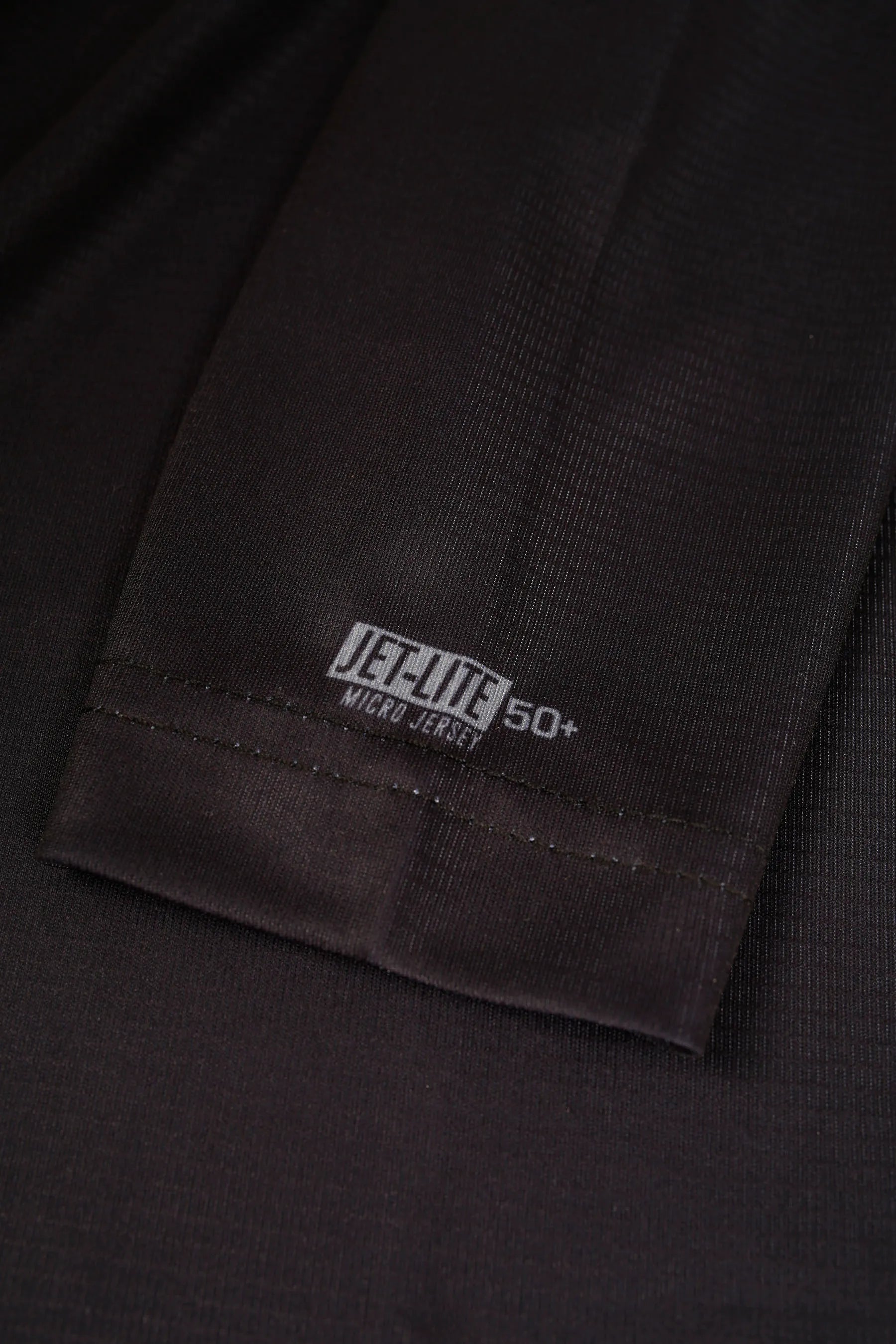 Close-up of a black fabric with 'JET-LITE' UPF 50+ logo and text on a dark background