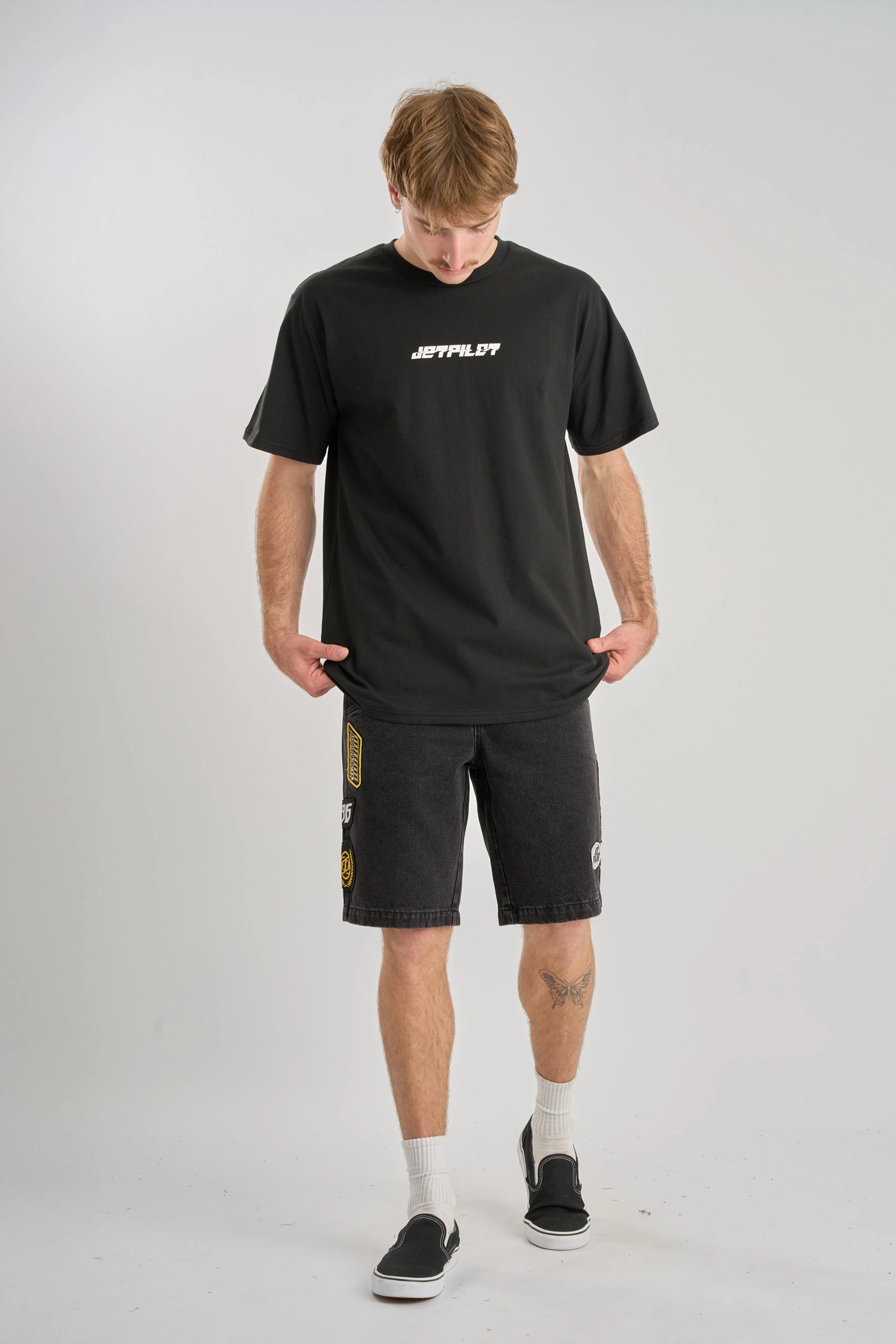 Man wearing a black Jetpilot Progressive t-shirt and shorts with a logo on a grey background — image 2