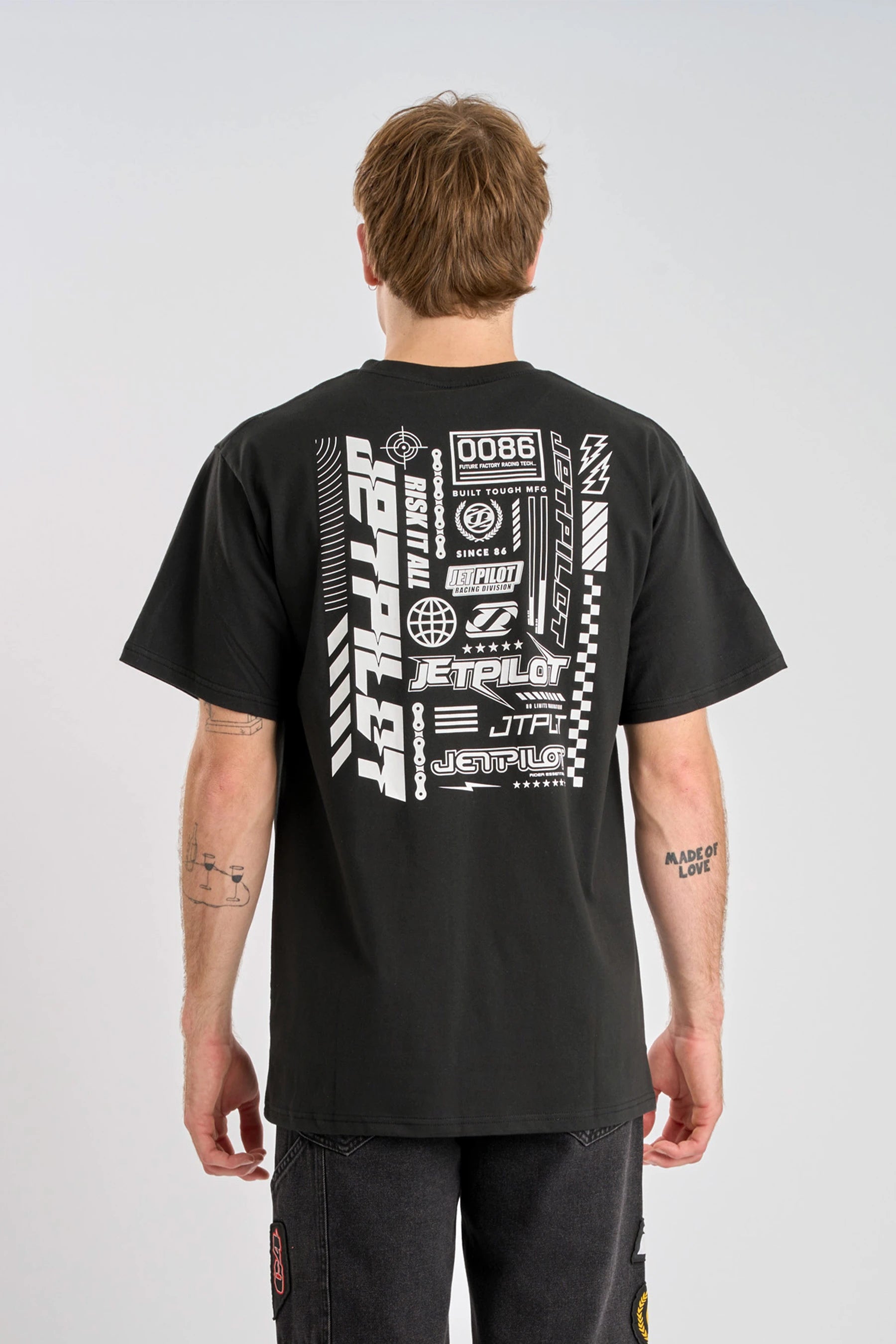 Person wearing a black Jetpilot Progressive t-shirt with white logo graphics and text on a plain background — image 2
