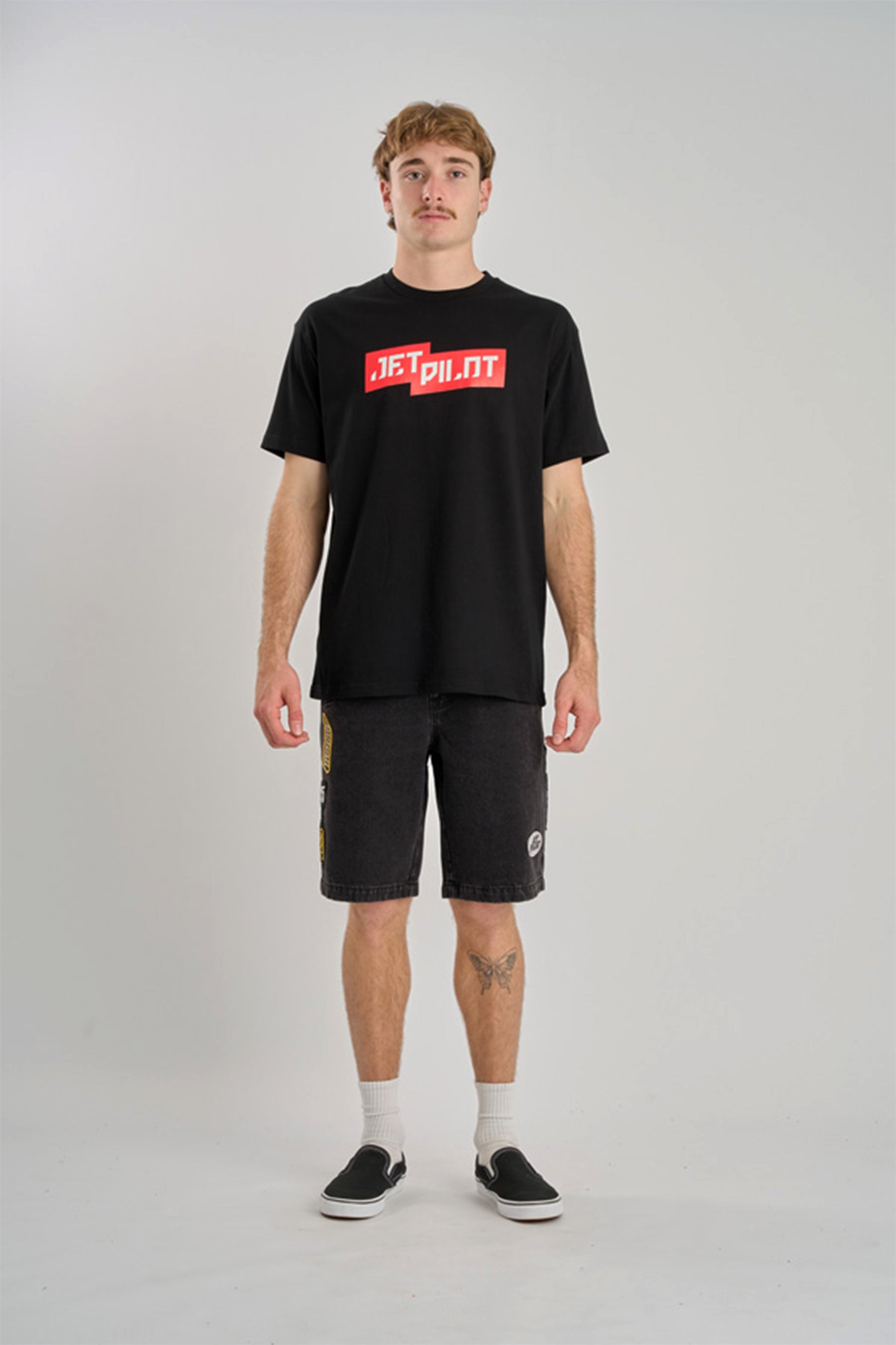 Person wearing a black t-shirt with red logo and black shorts on a gray background