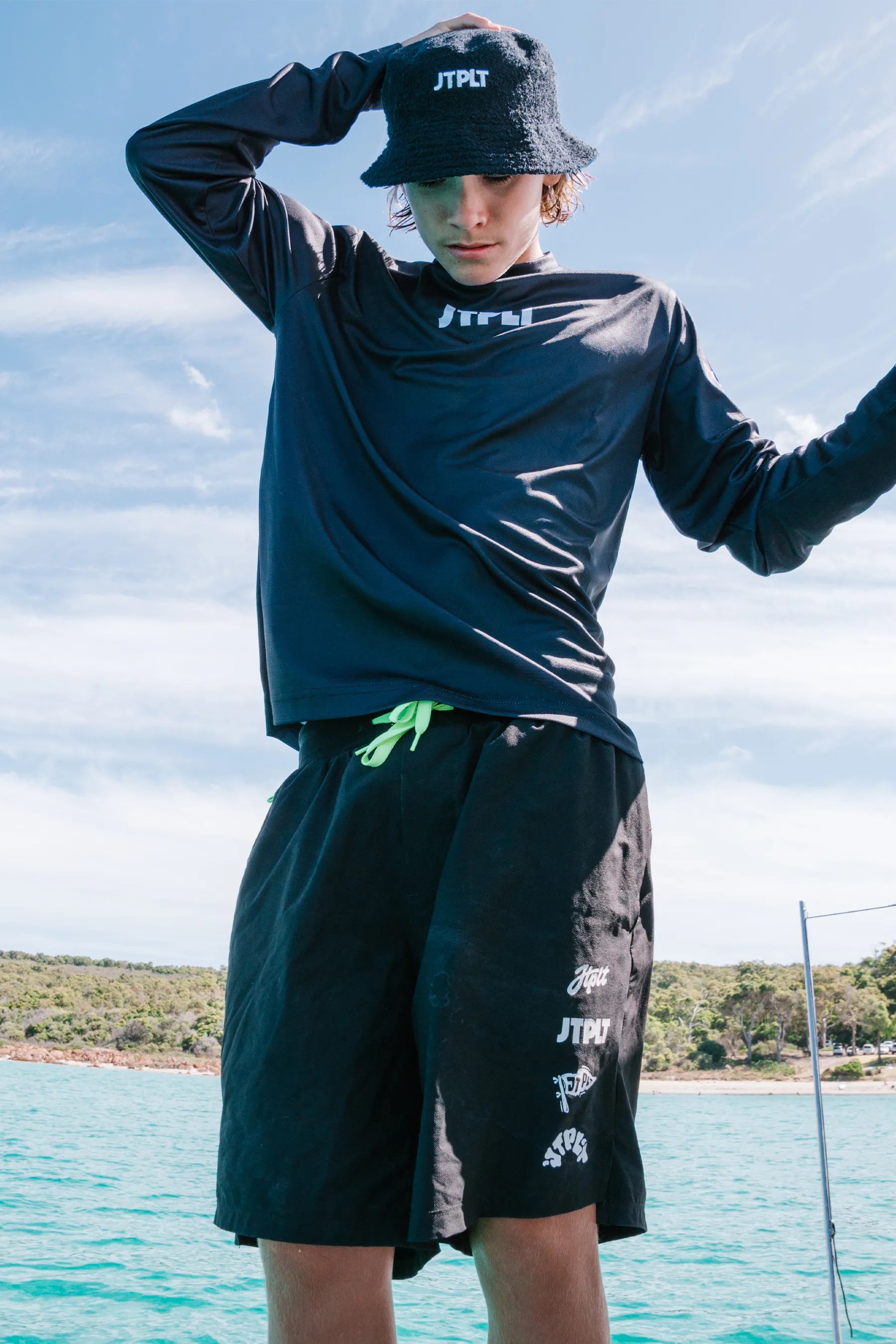 Person wearing a black long-sleeve shirt and shorts with visible branding, standing by a body of water.