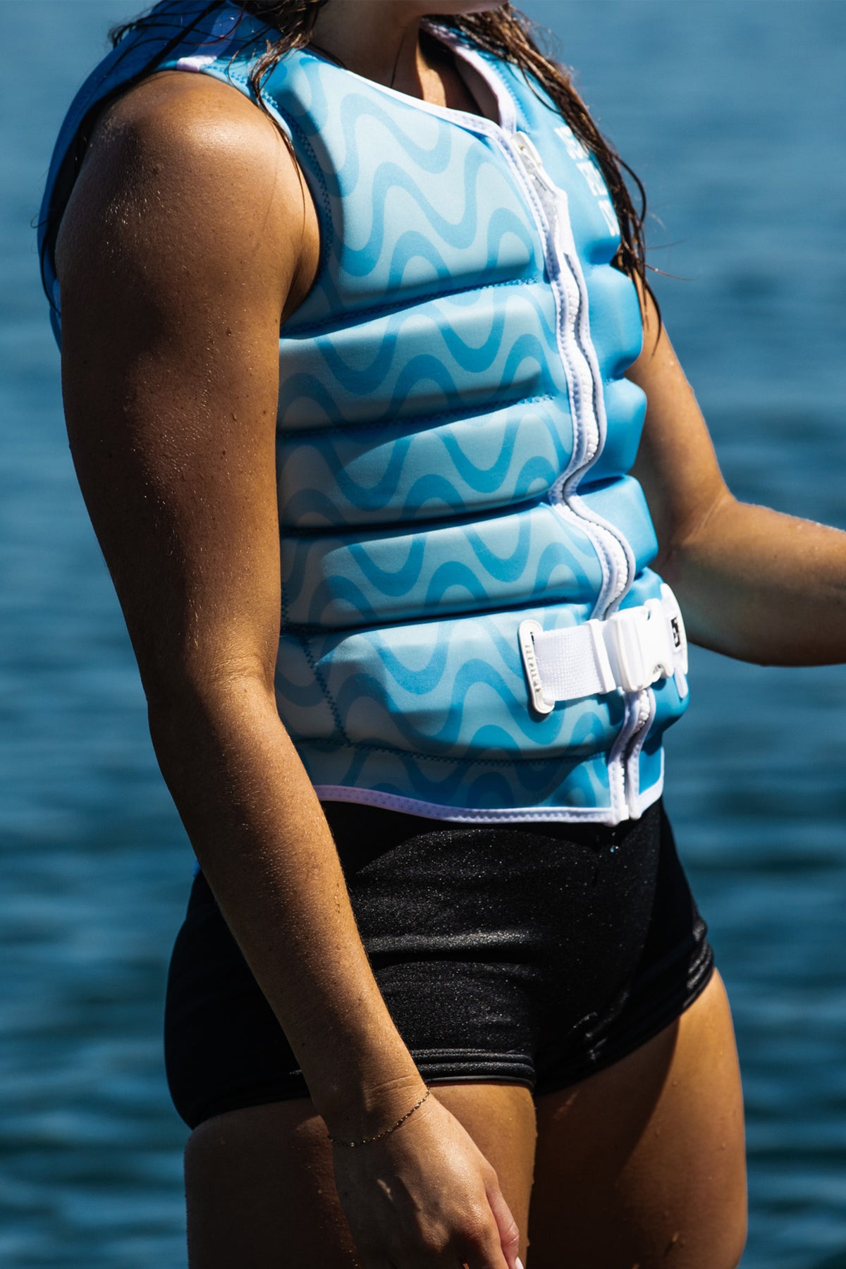 Model standing by the water in the Blue Luna life jacket, with waves printed across the front panels
