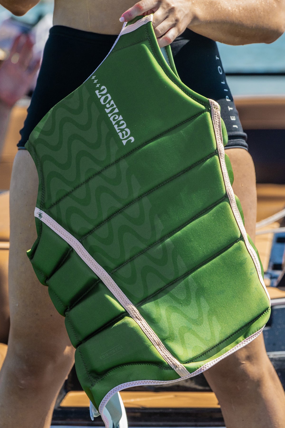 Model holding up the Olive Luna on the boat, showing the back wave print and peach binding