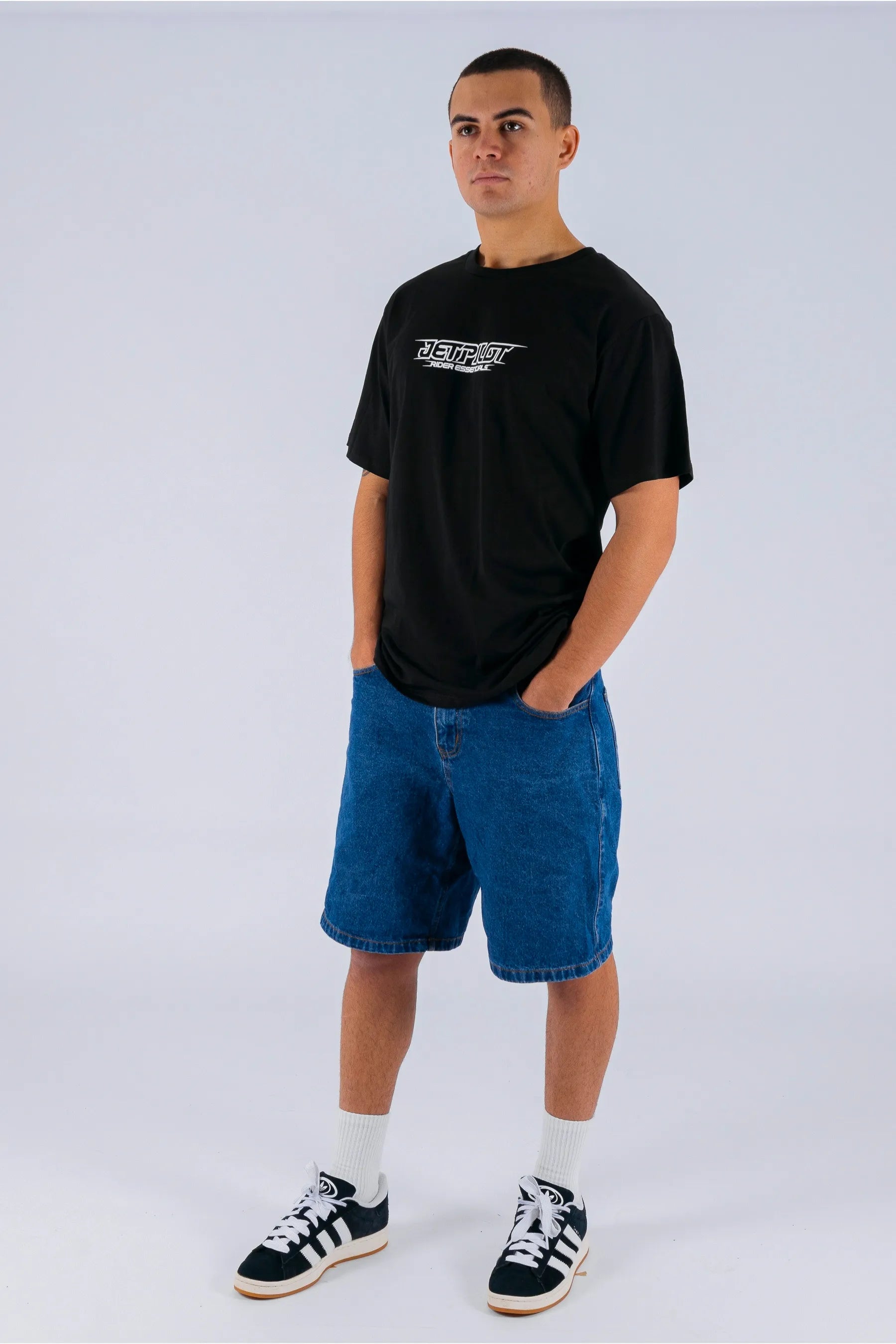 a person wearing a black tee with a Jetpilot logo, blue shorts and a black/white shoes — view 3 (3)