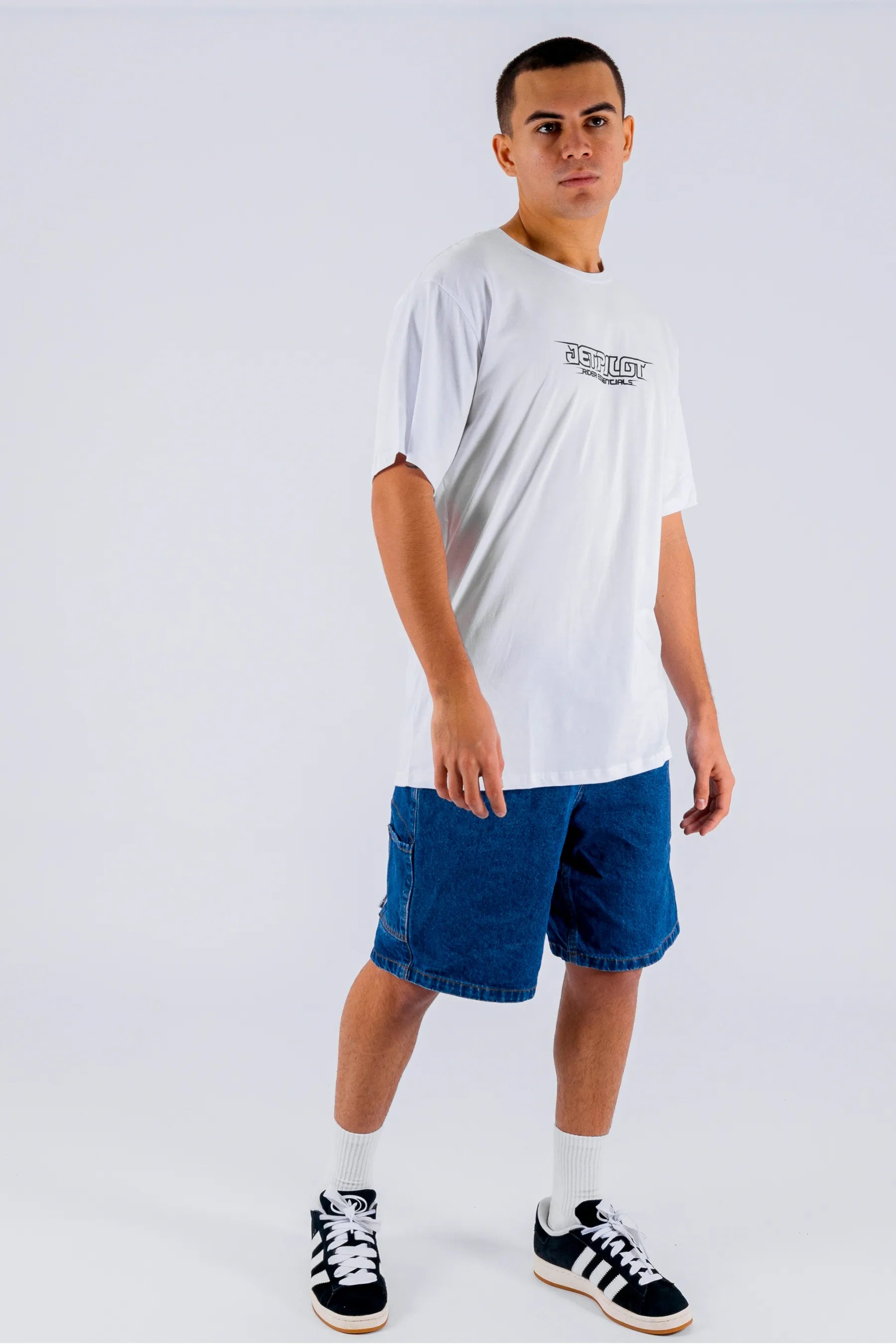 a person wearing a white tee with a Jetpilot logo, denim short and black/white shoes on a white background — view 5 (3)
