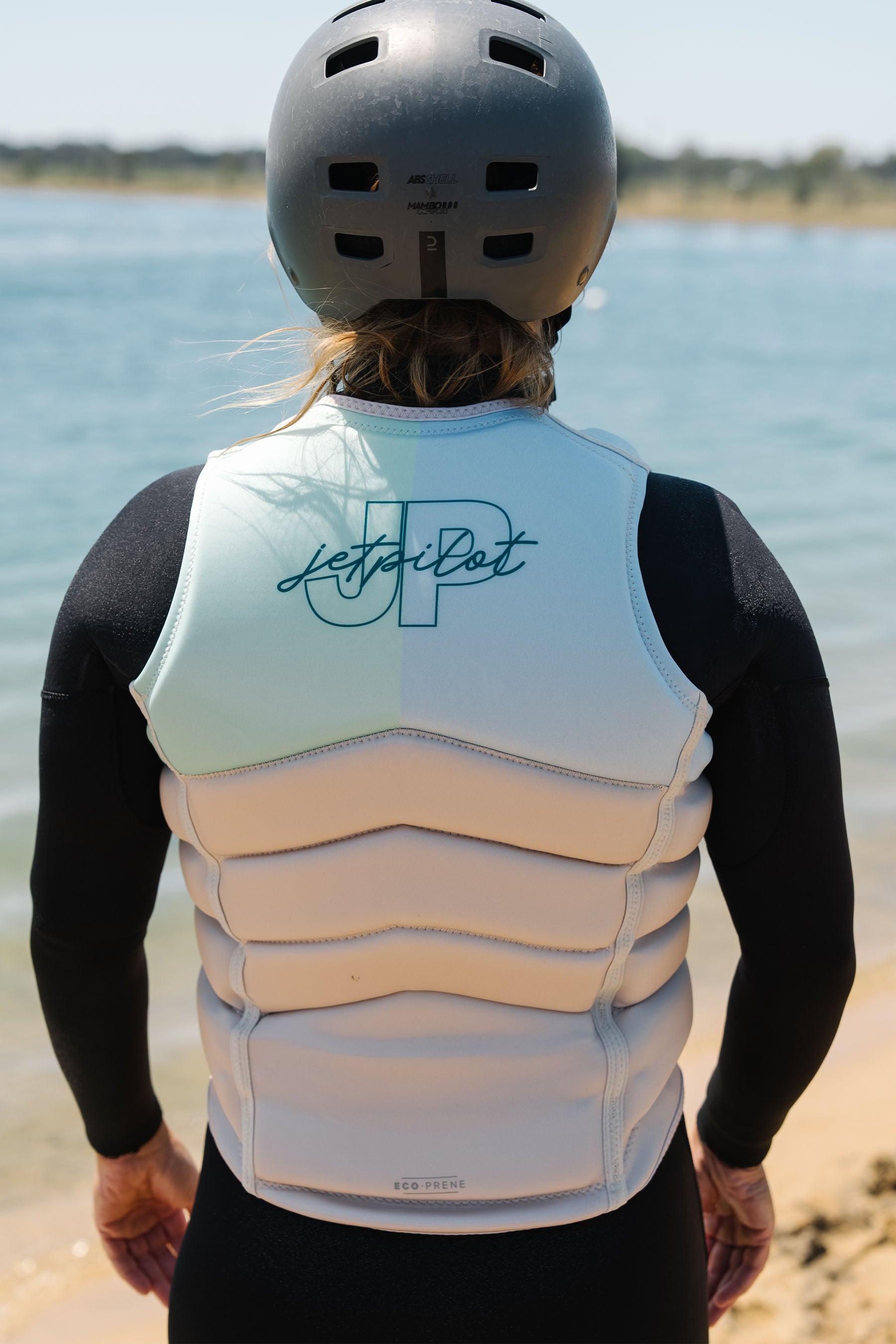 Person wearing a light blue and beige life vest with 'JP' branding on a beach.